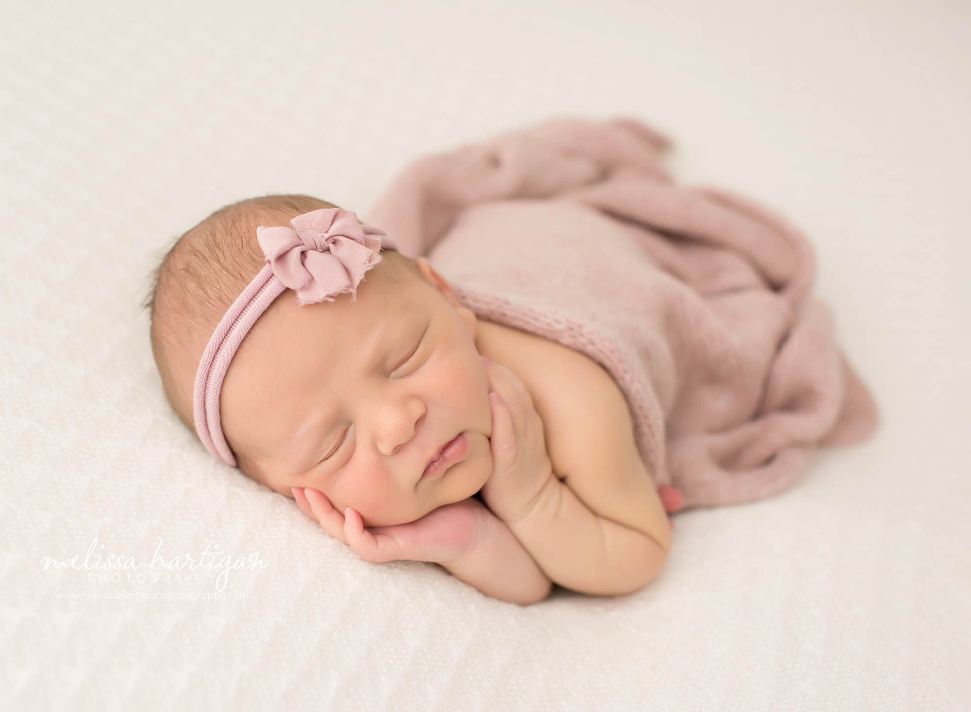 newborn baby girl posed on side wearing pink bow headband and pink wrap draped over windsor CT newborn photography