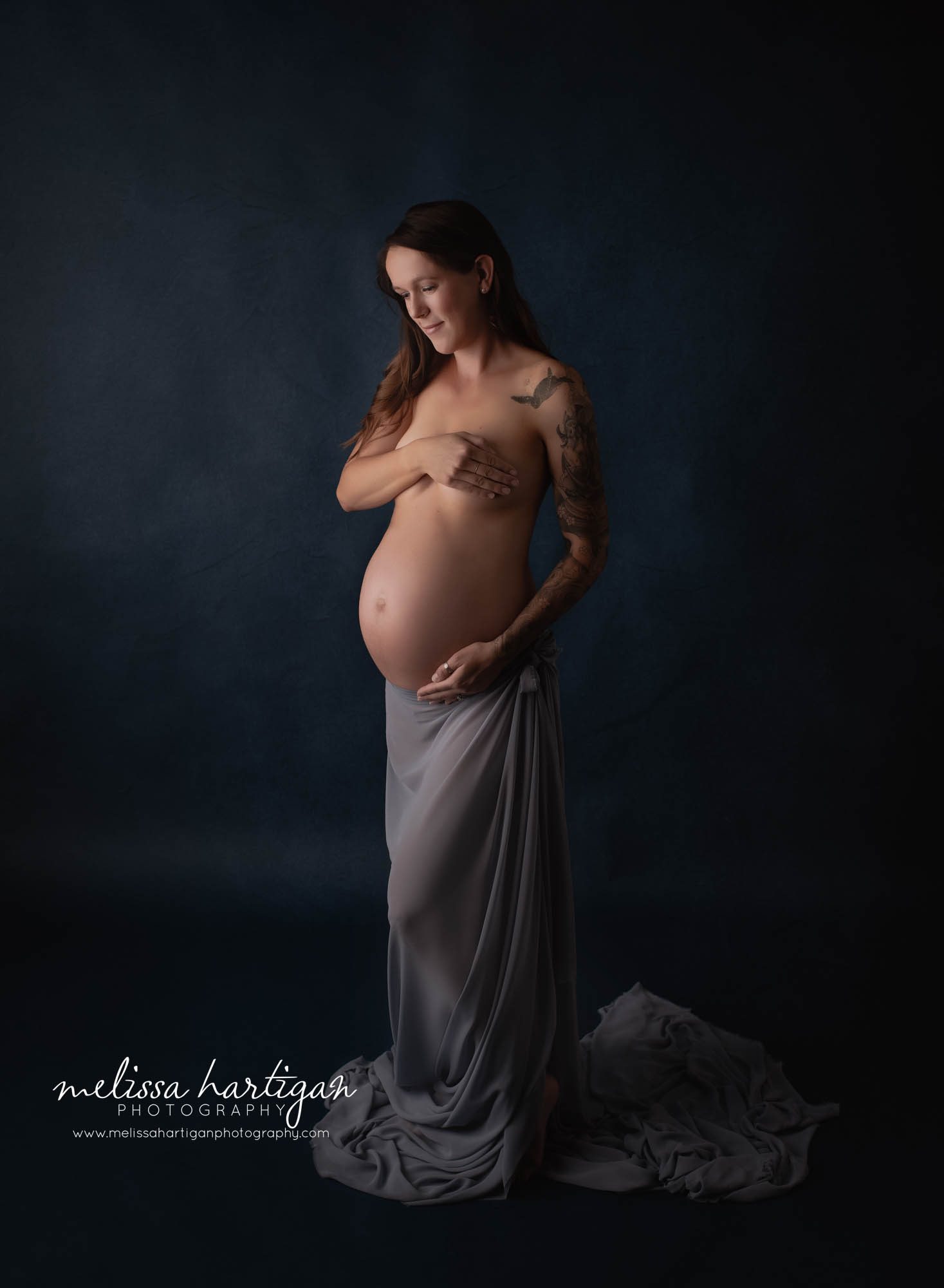pregnant mom looking down at pregnant belly wearing draped fabric studio maternity