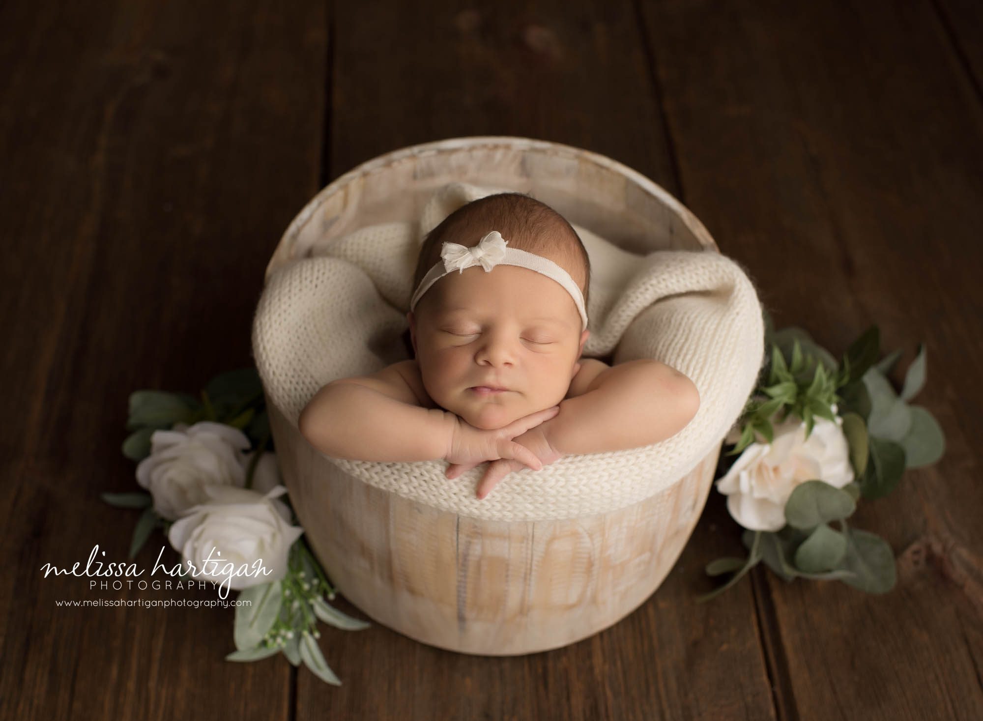 newborn baby girl posed in wooden barrel with cream knitted wrap wearing cream bow headband