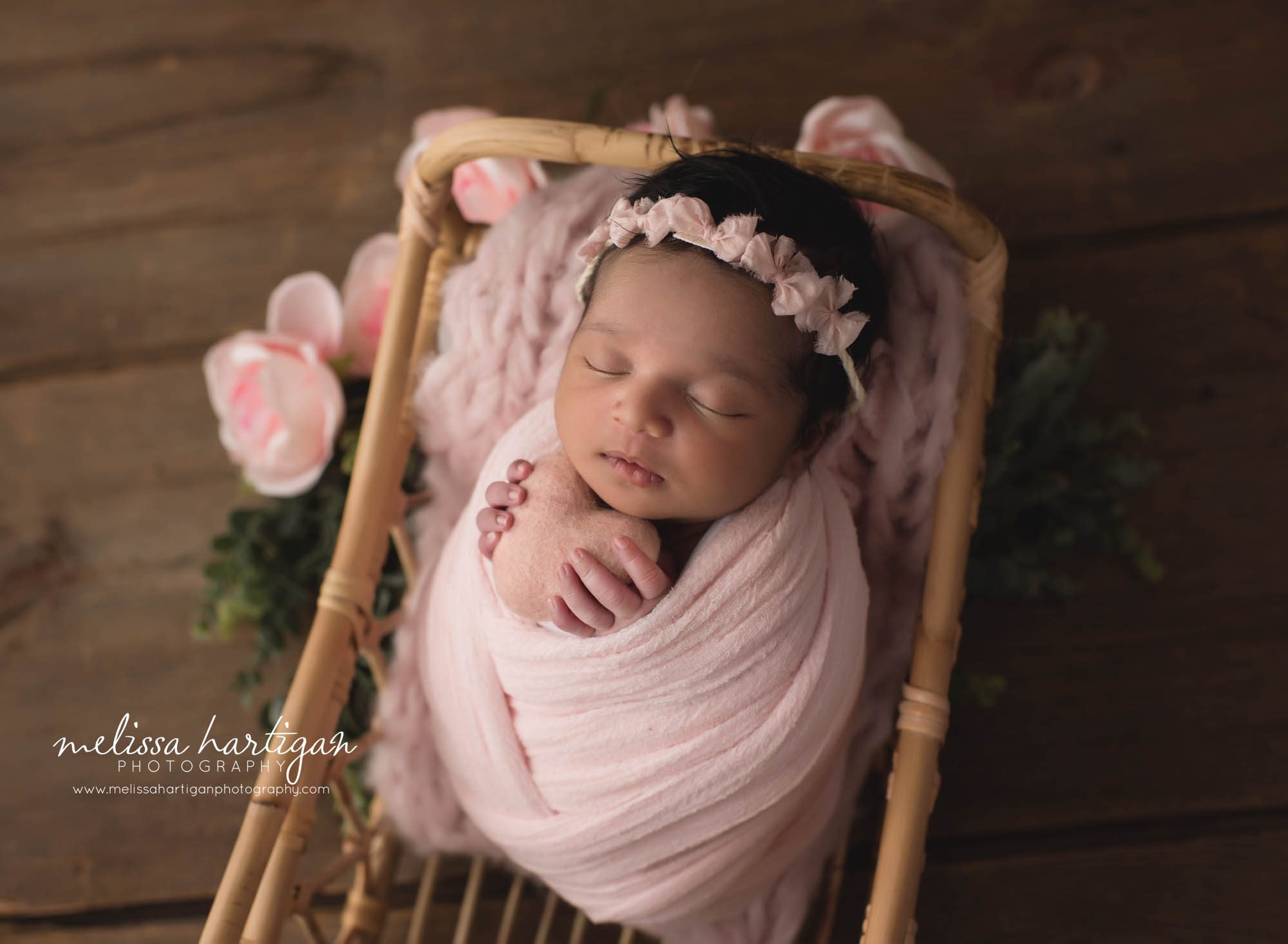 newborn baby girl wrapped in pink wrap holding pink felted heart prop