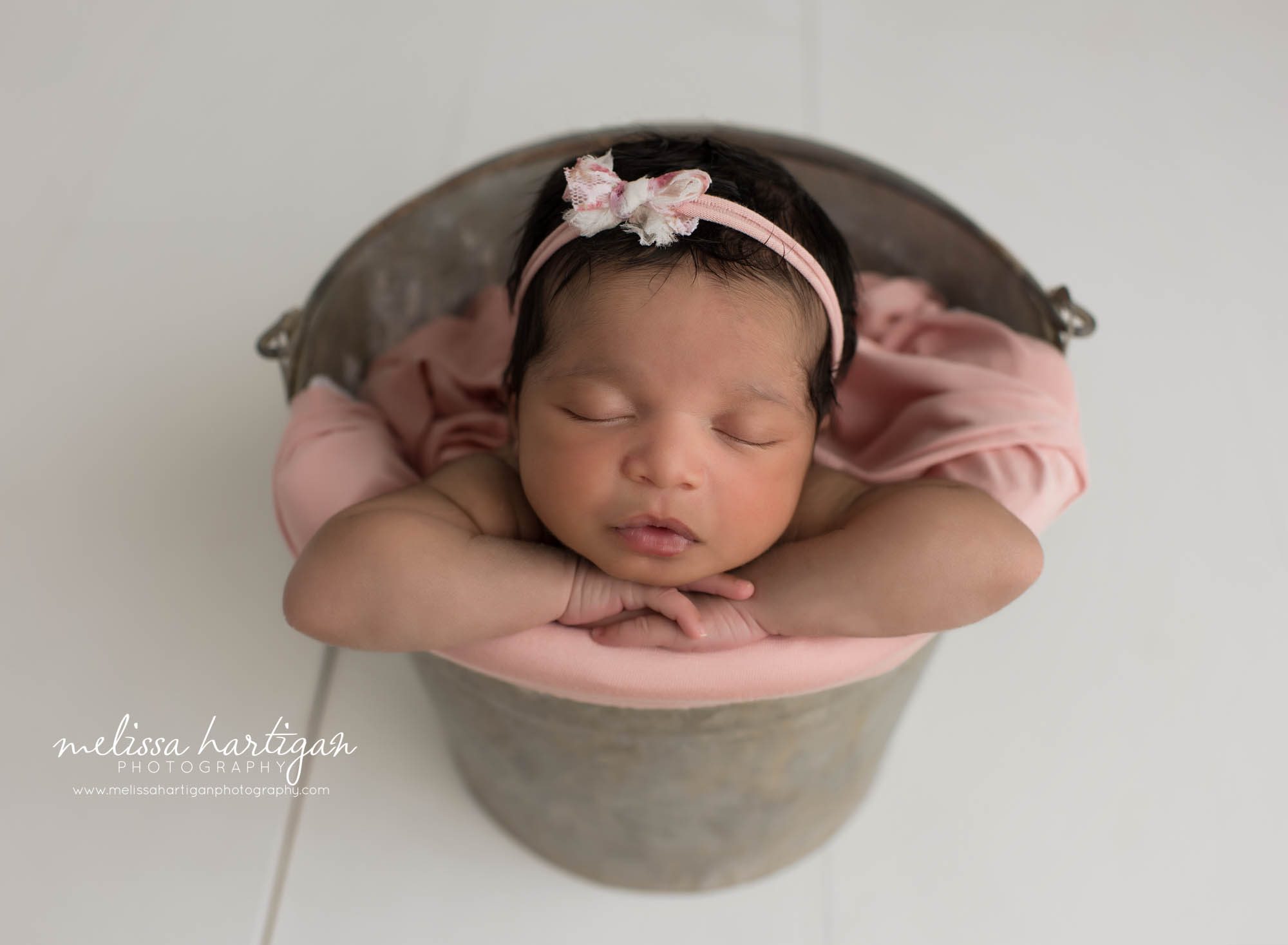 newbonr baby girl posed in metal bucket with pink and cream bow headband hamden CT newborn Photography