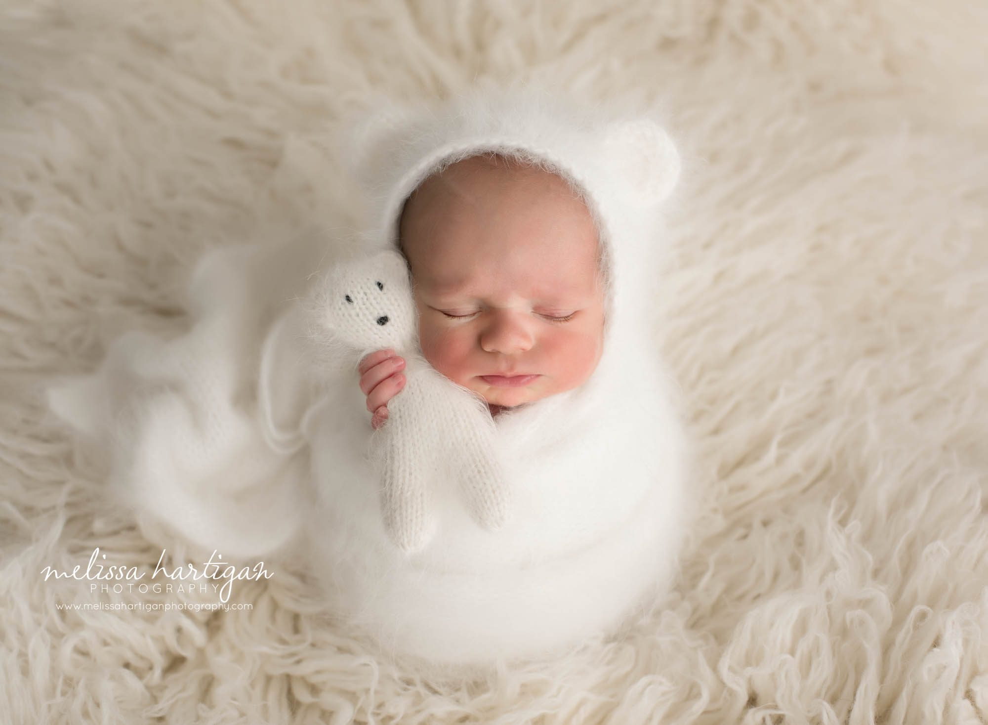 newborn baby boy wrapped in knitted wrap white posed on cream flokati