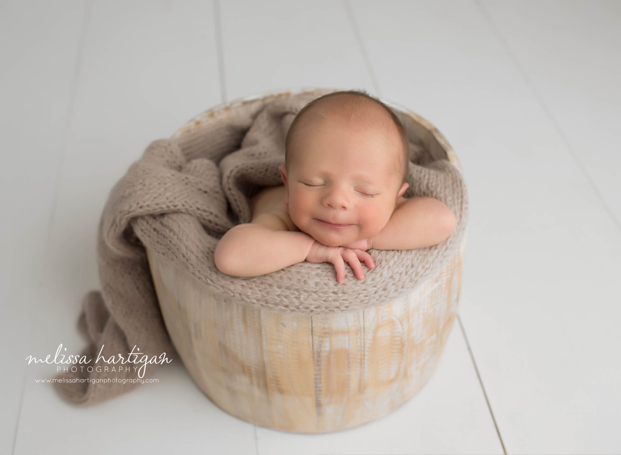 newborn baby boy posed in wooden barrel sleeping smiling smirk on his face