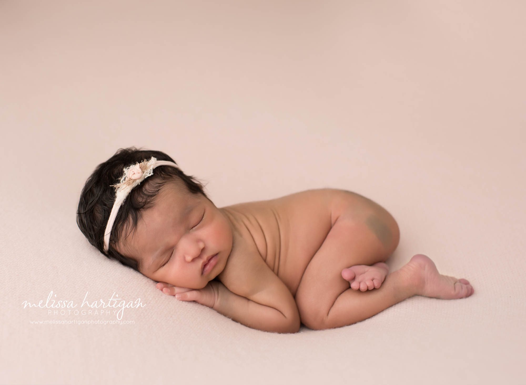 newborn baby girl posed on tummy with pink flower headband