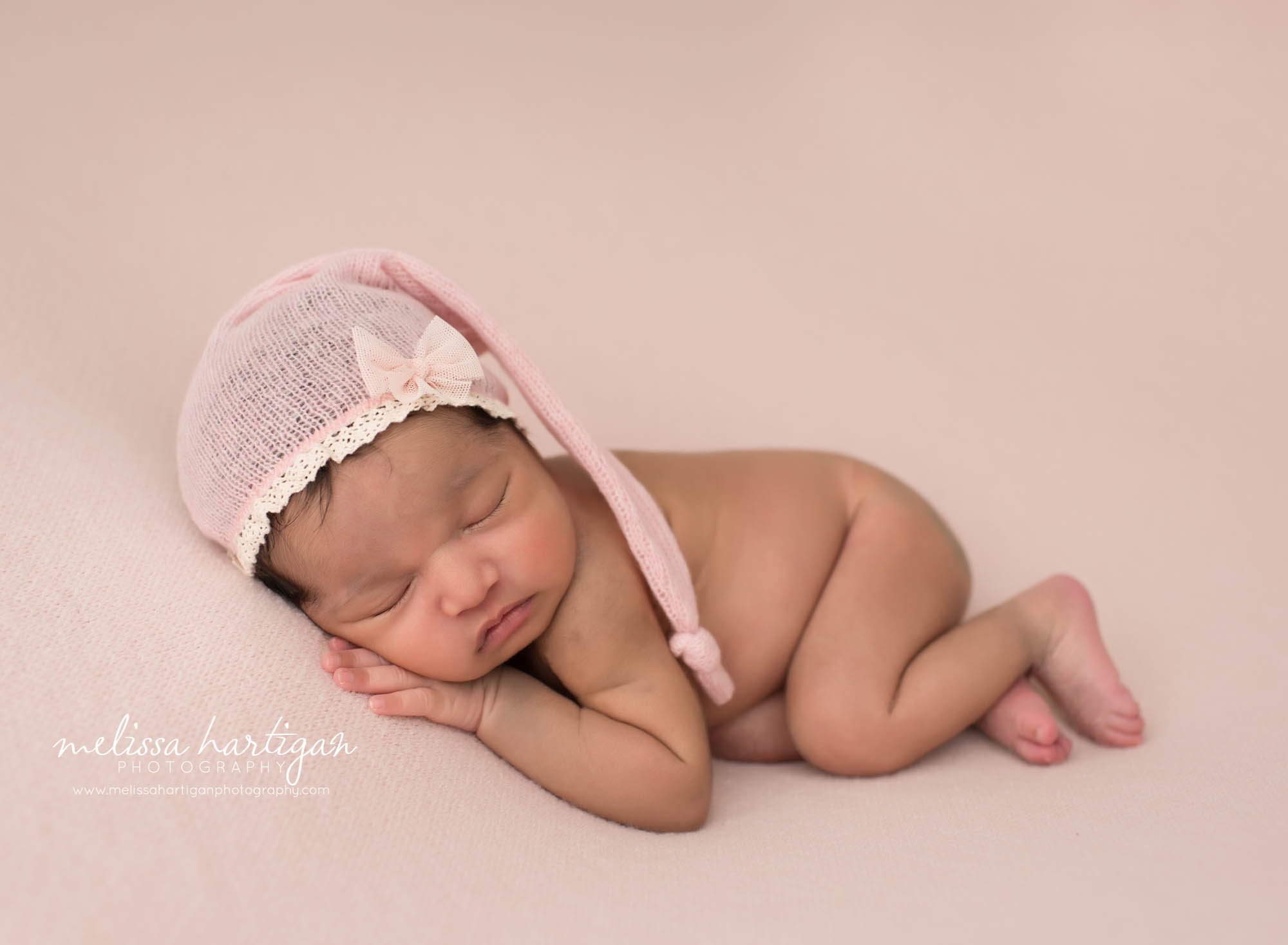 newborn baby girl posed on tummy wearing pink lace sleepy cap