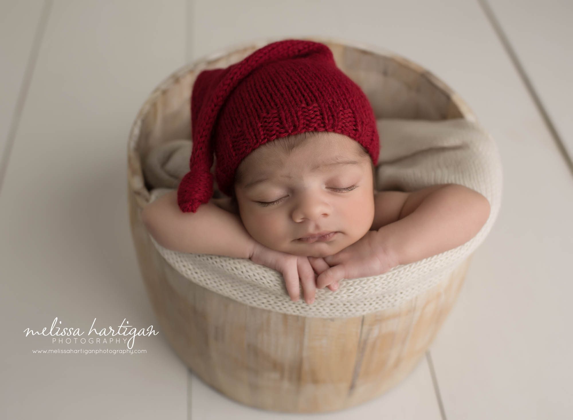 newborn baby boy posed in wooden barrel wearing red knitted hat