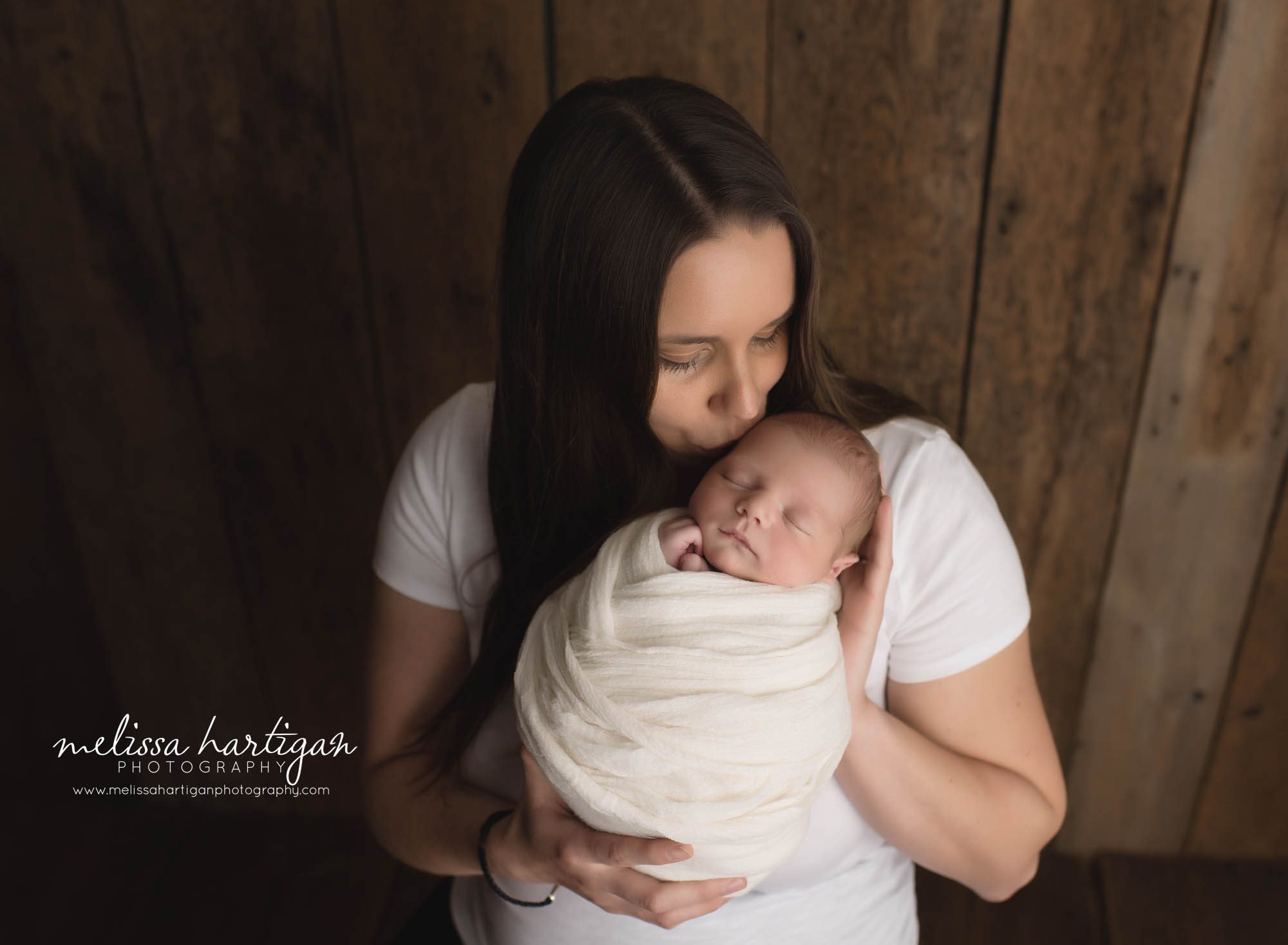 mom holding baby boy kissing him on forehead parents pose newborn photography CT