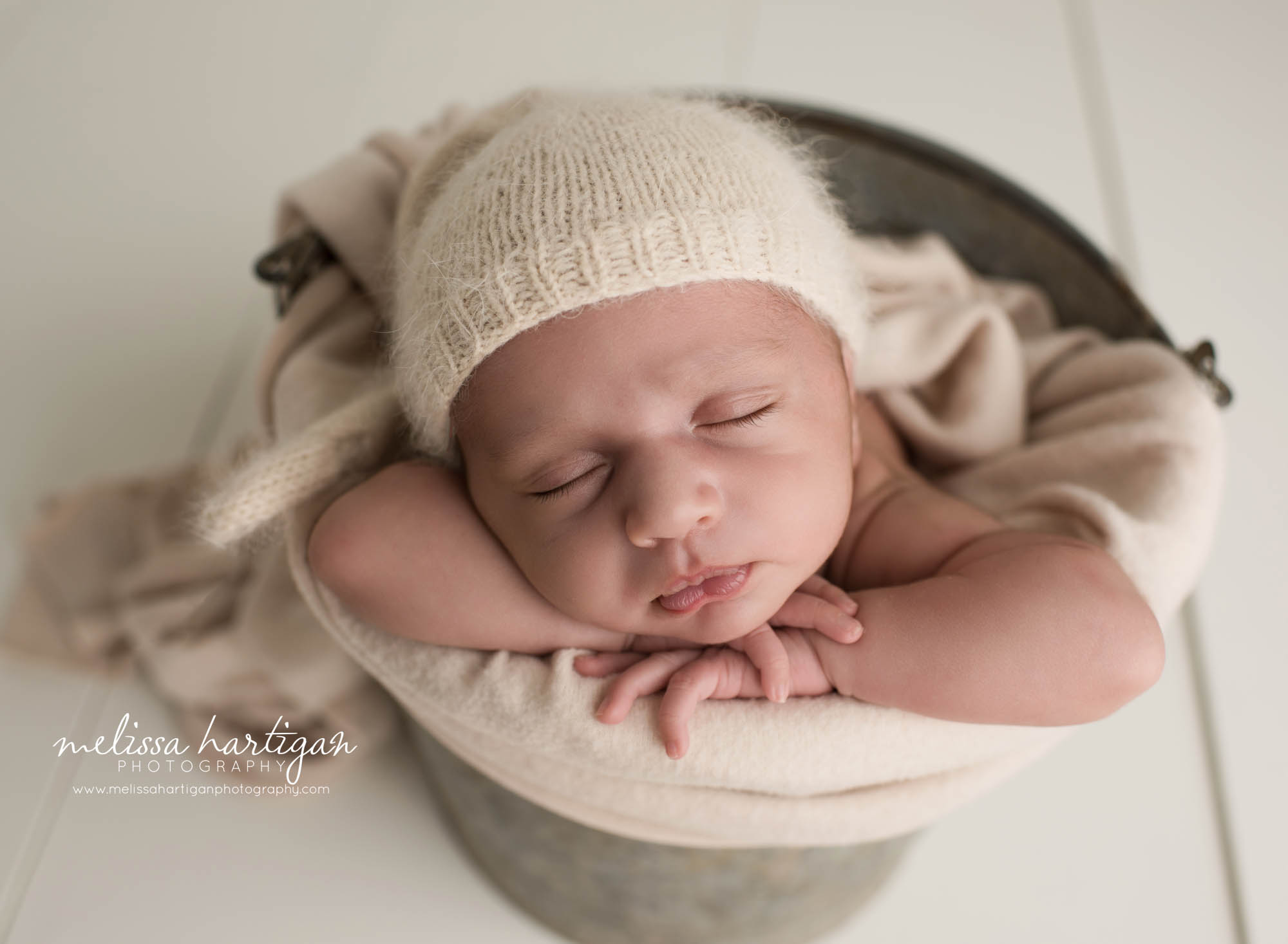 newborn baby boy posed in metal bucket with tan colored layer and knitted sleepy cap