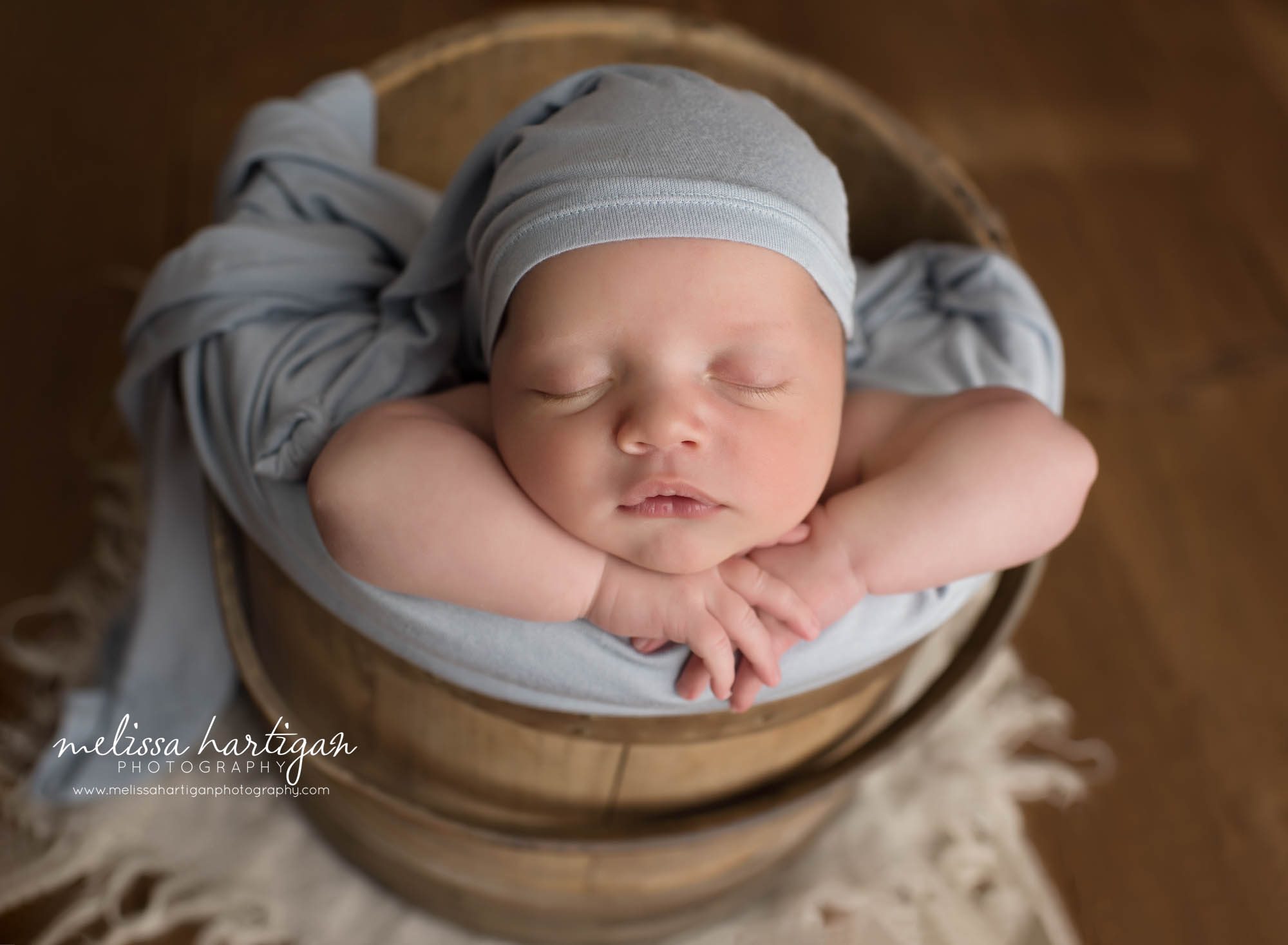 newborn baby boy posed in wooden bucket wearing light blue sleepy cap tolland county CT newborn photography
