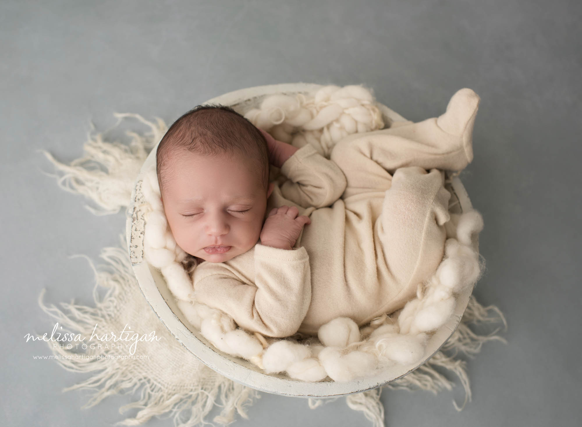 newborn baby boy posed in cream bowl wearing light tan colored footed sleeper