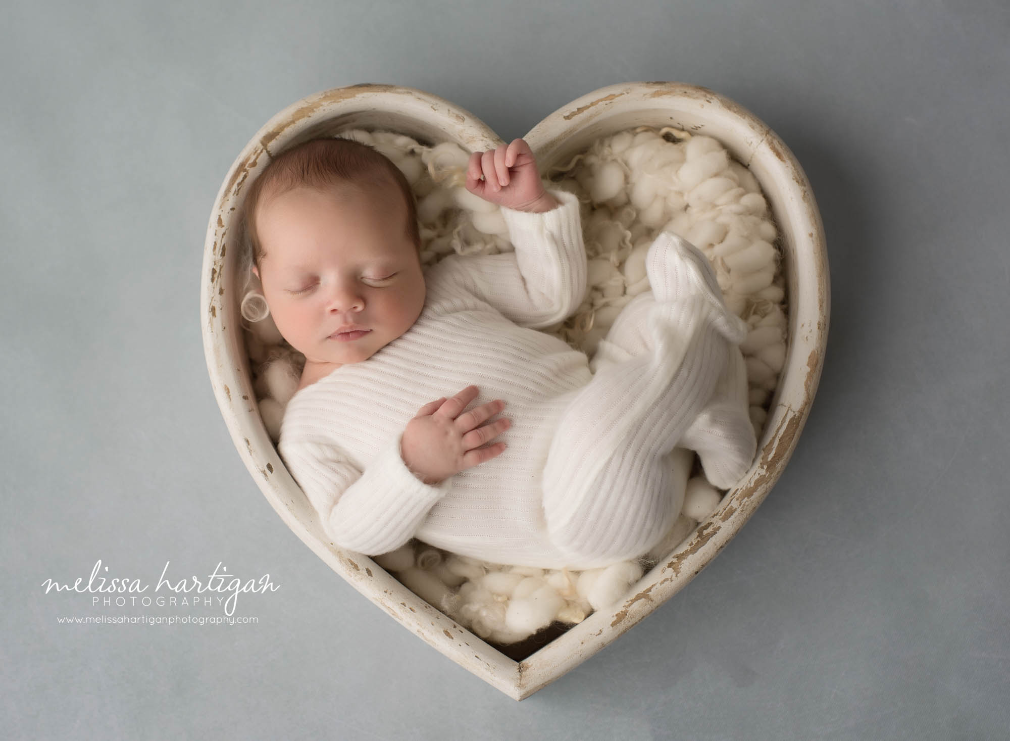 newborn baby boy posed in cream wooden heart prop bowl wearing cream footed newborn sleeper CT newborn photographer