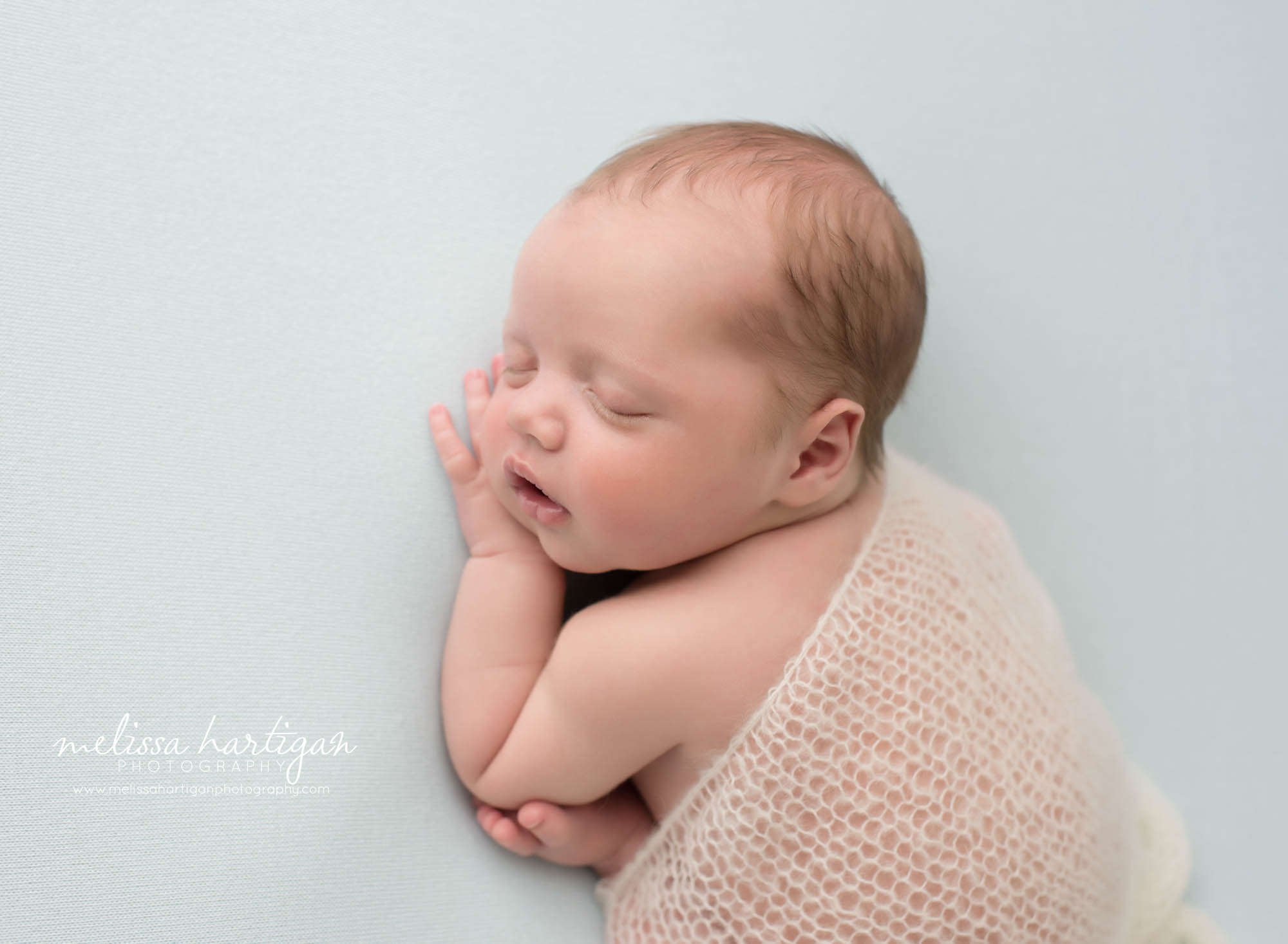 Newborn baby boy posed on tummy with knitted drape layer