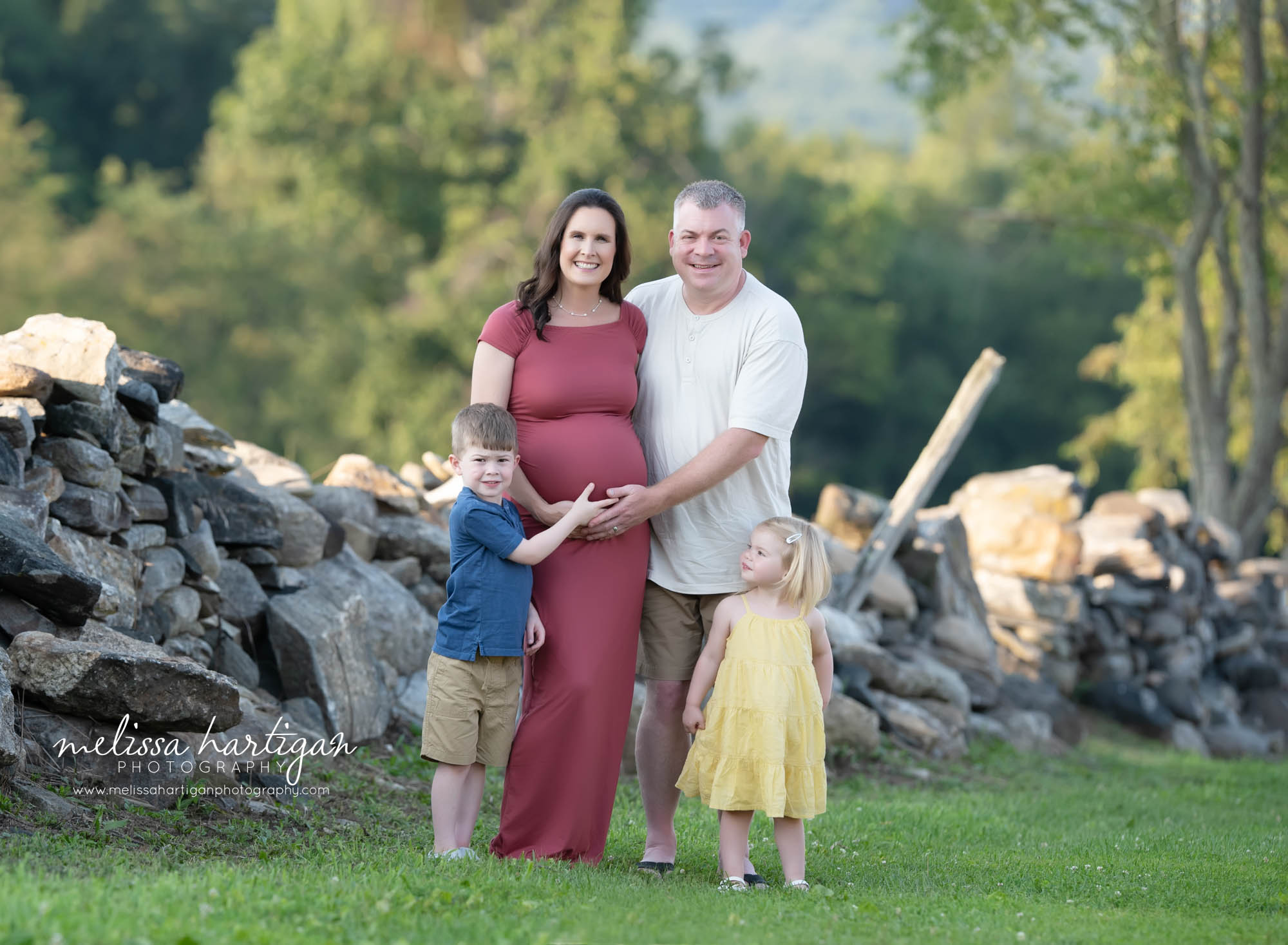 mom dad brother sister looking at holding baby belly outside family maternity picture