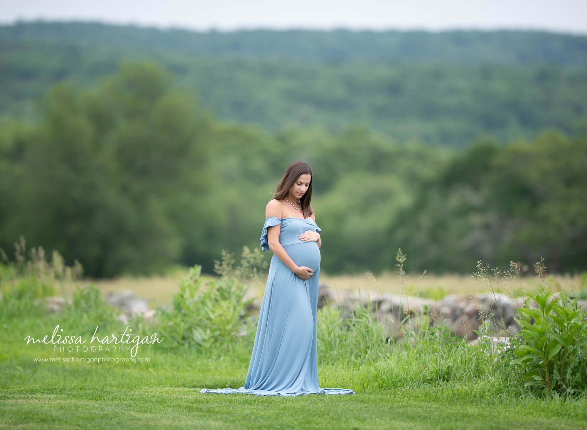 pregnant mom holding baby belly wearing blue maternity dress outside maternity session 