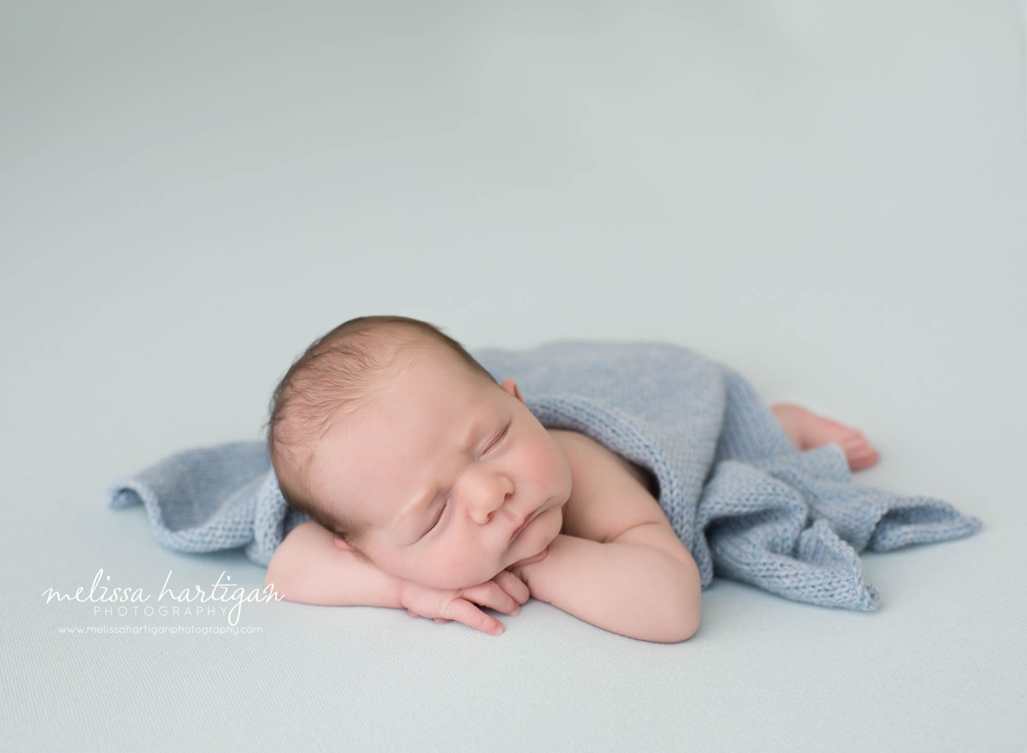 newborn baby boy posed on light blue backdrop with blue knitted layer draped over his back CT newborn photography