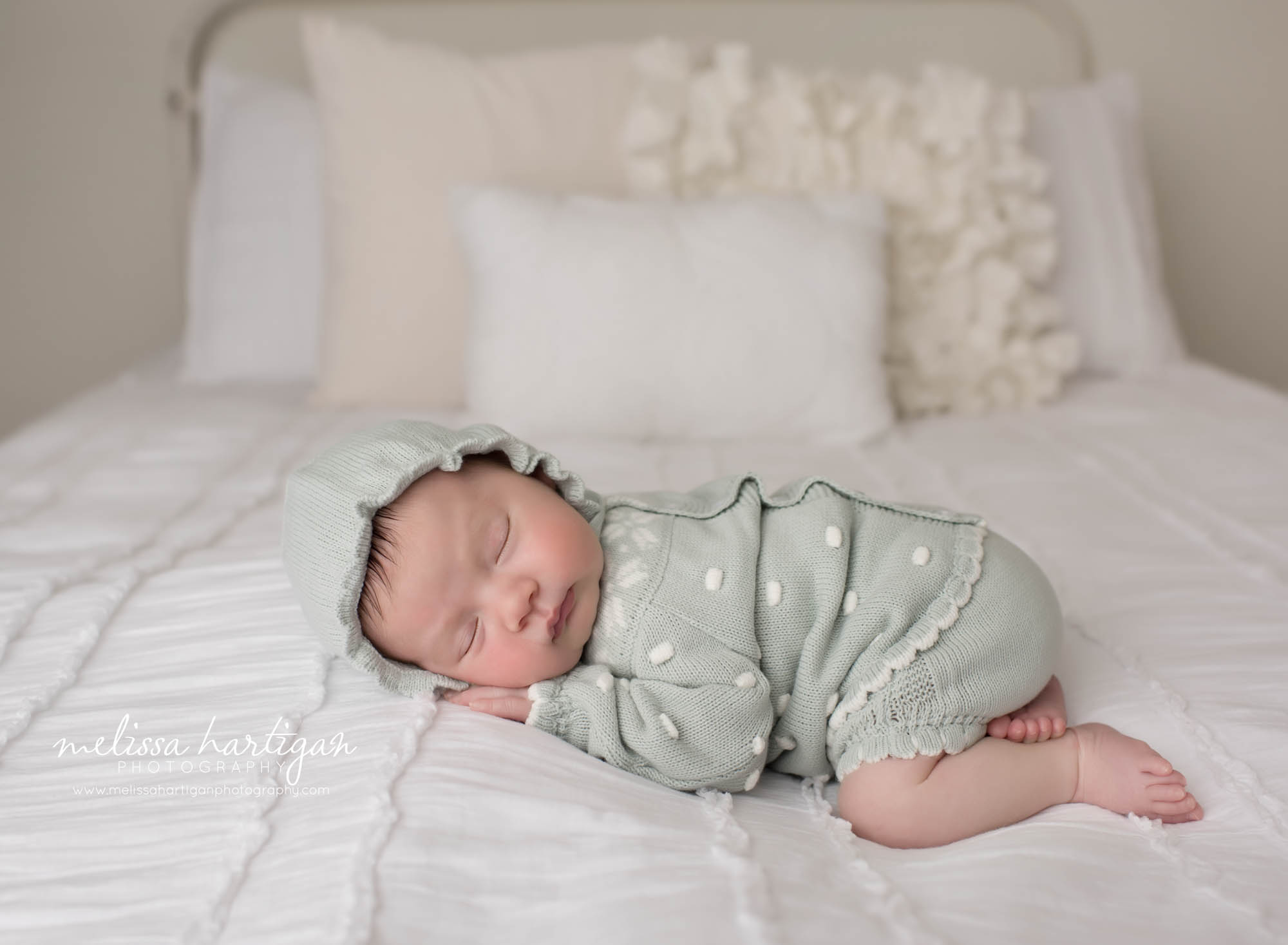 newborn baby girl posed on tummy on bed set up wearing baby bonnet
