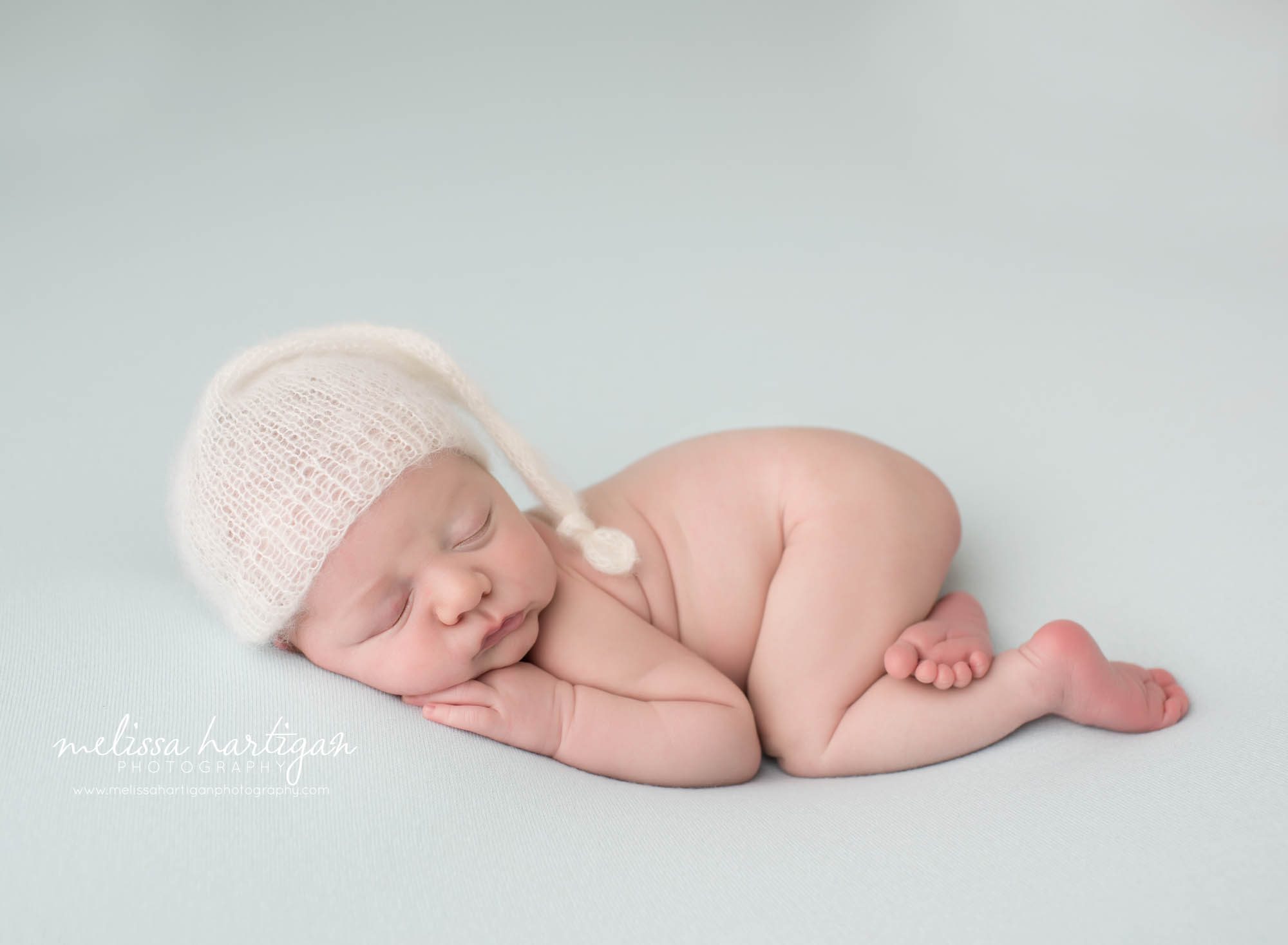 newborn baby boy posed on tummy with bum up wearing knitted cream colored sleepy cap newborn photography east windsor