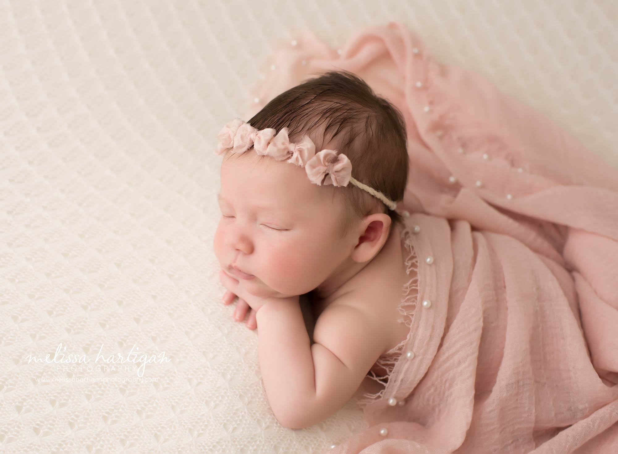 newborn baby girl posed on tummy wearing bow headband and pink wrap draped over