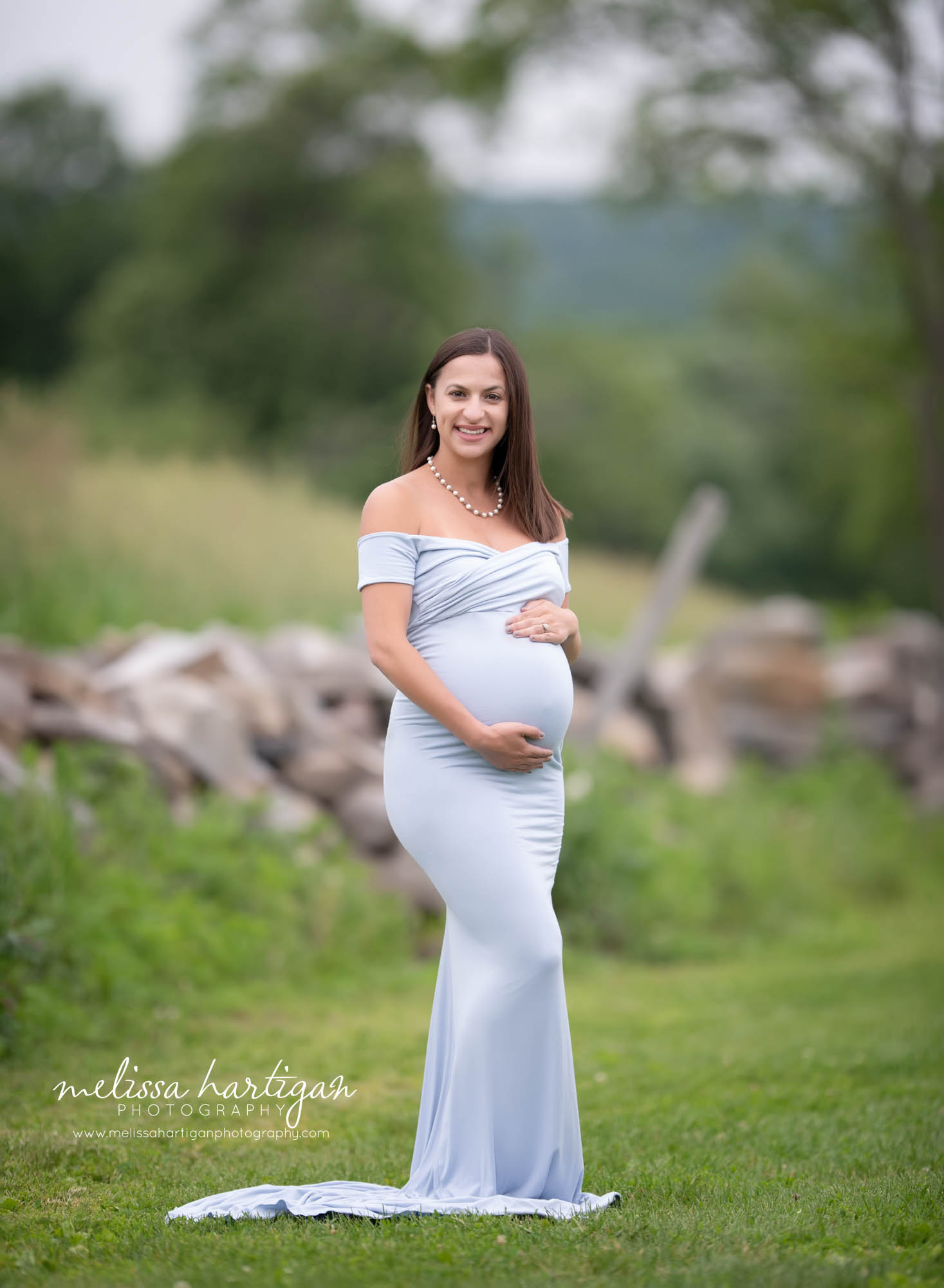 mom to be holding baby bump wearing light blue off the shoulder maternity dress