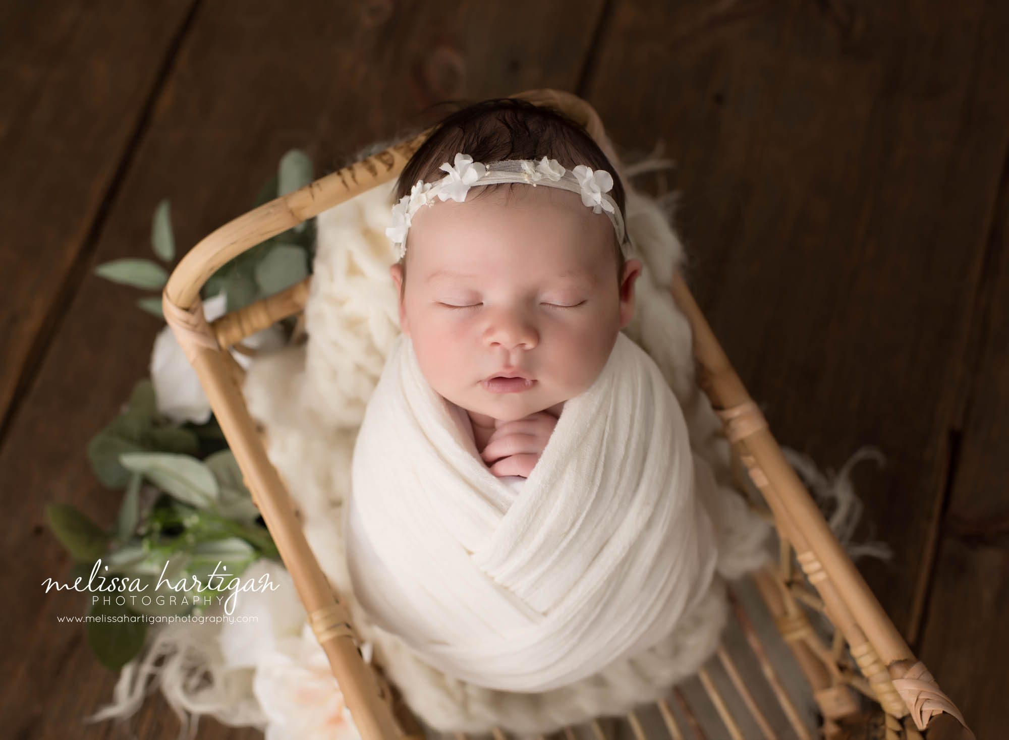 newborn baby girl posed in basket wrapped in cream wrap