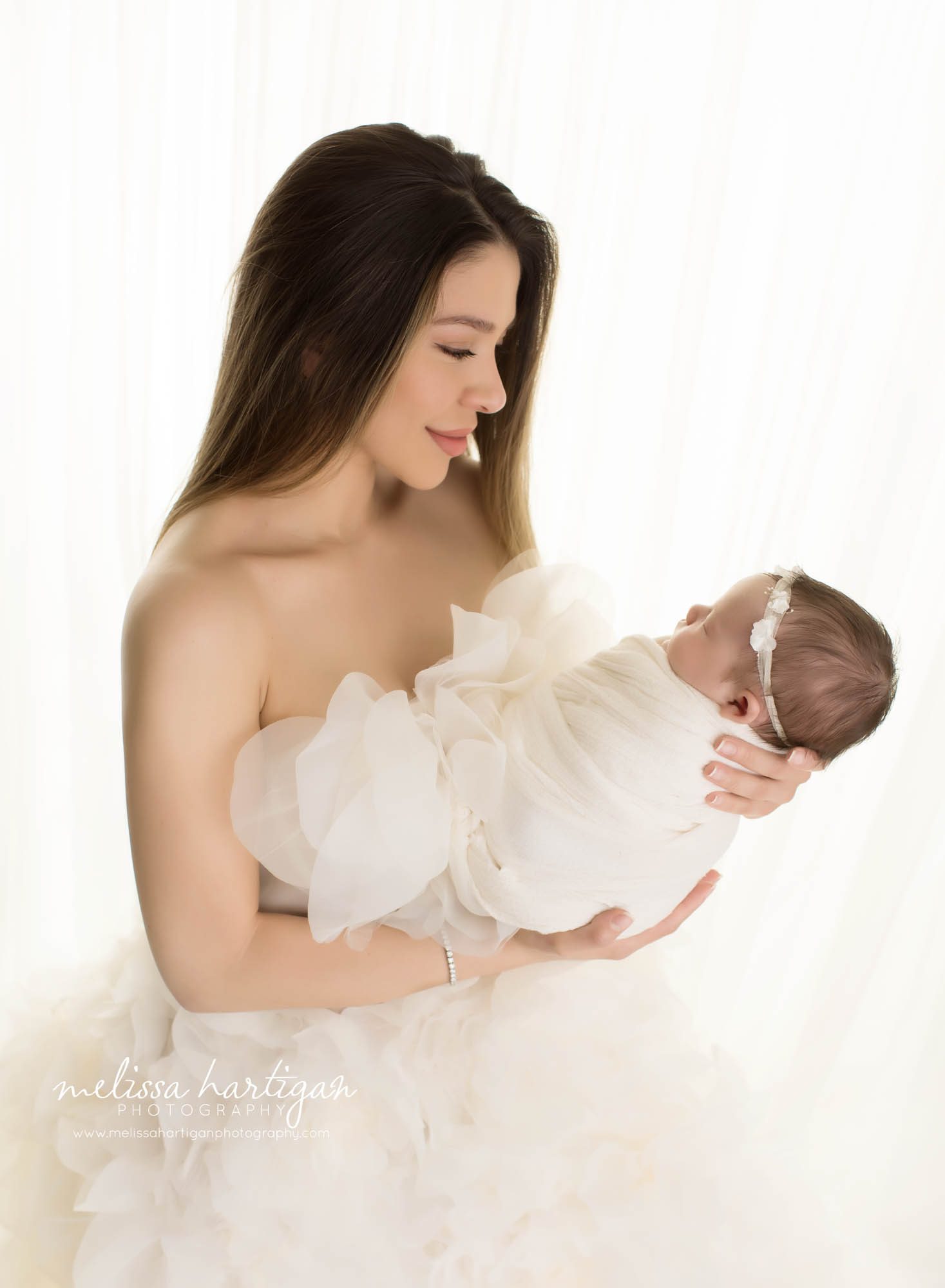 mom holding newborn baby girl wearing cream wrap and cream ruffled dress