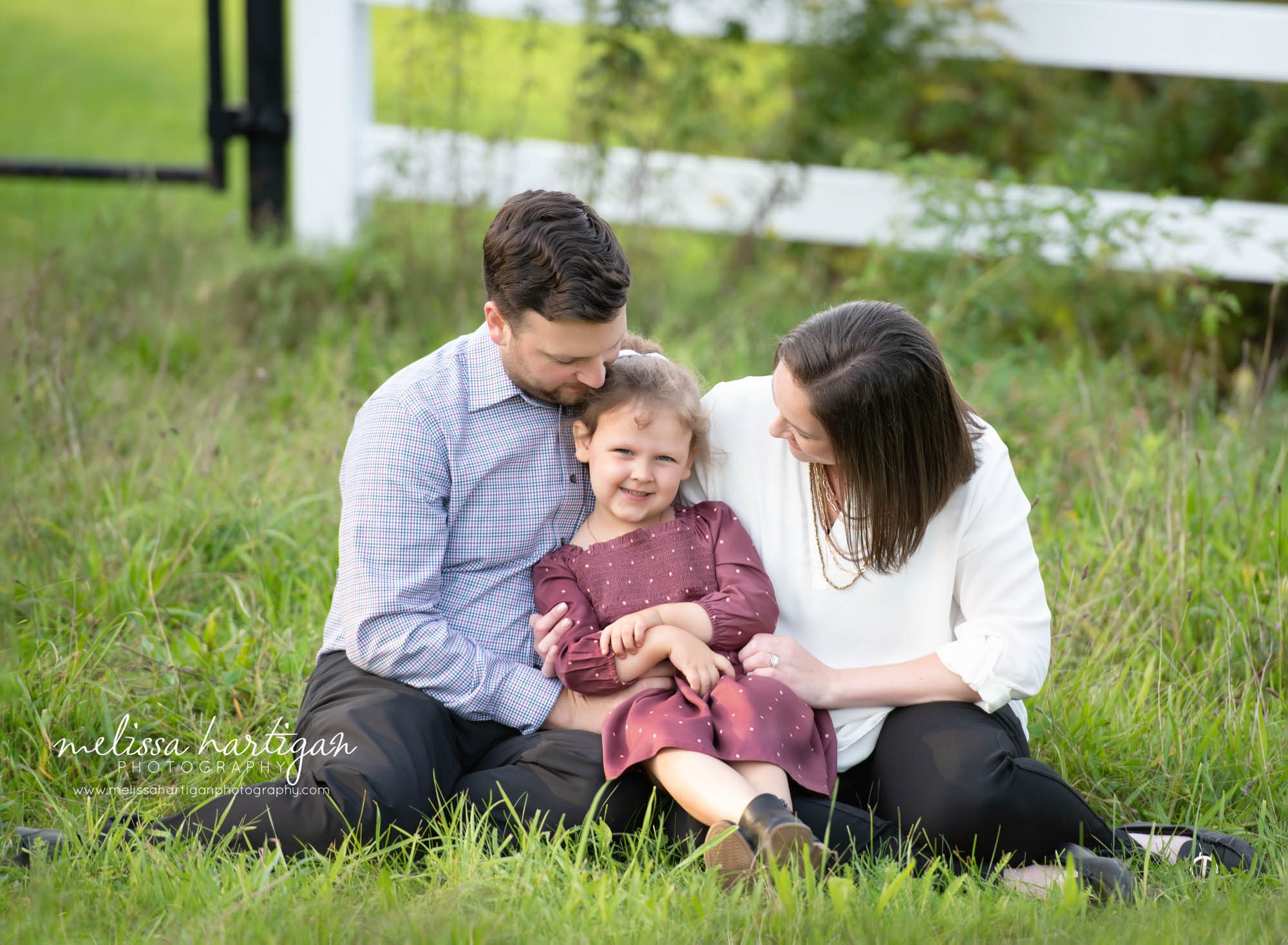 mom dad daughter sitting on grass little girl smiling family photography