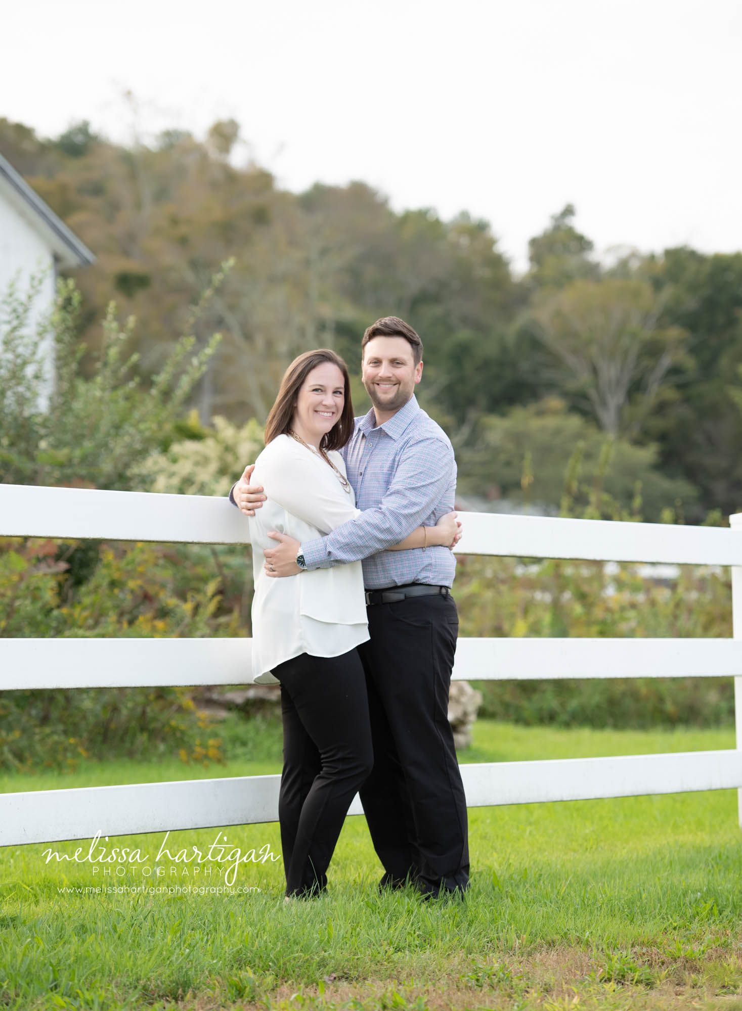 couple pose standing against white fence
