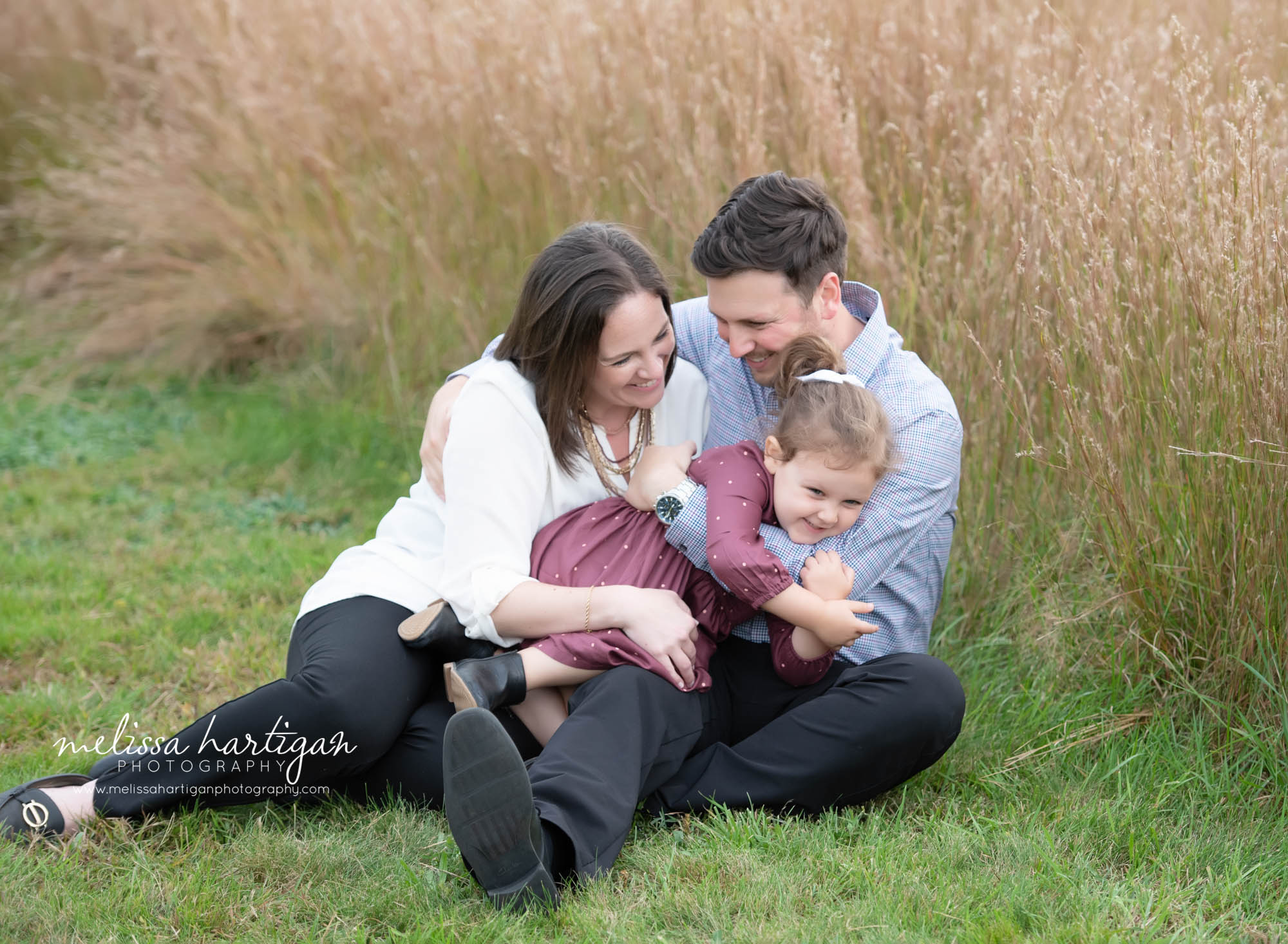 mom dad and daughter sitting on grass family photography pose