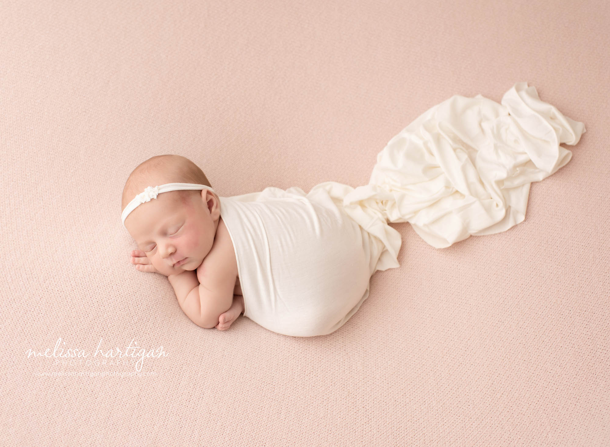 newborn baby girl posed on pink backdrop on tummy with cream wrap draped over