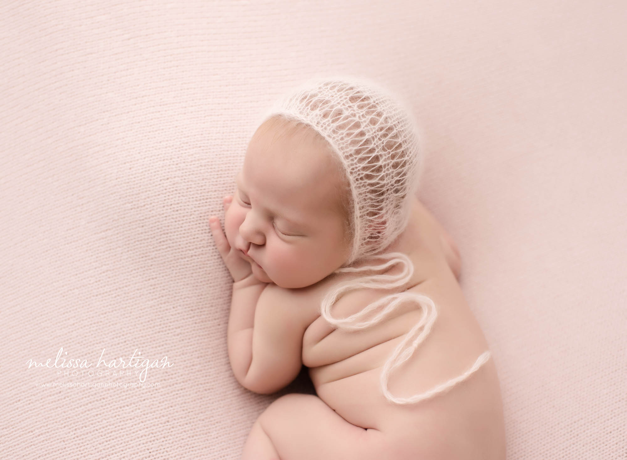 newborn baby girl posed on pink backdrop wearing knitted bonnet