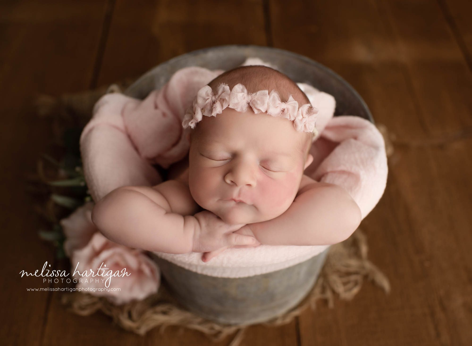 newborn baby girl posed in bucket with pink bow headband and pink drape wrap