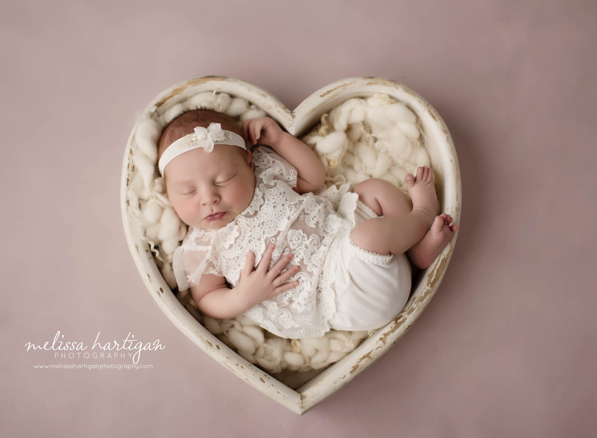 newborn baby girl wearing white lace outfit posed in wooden cream prop