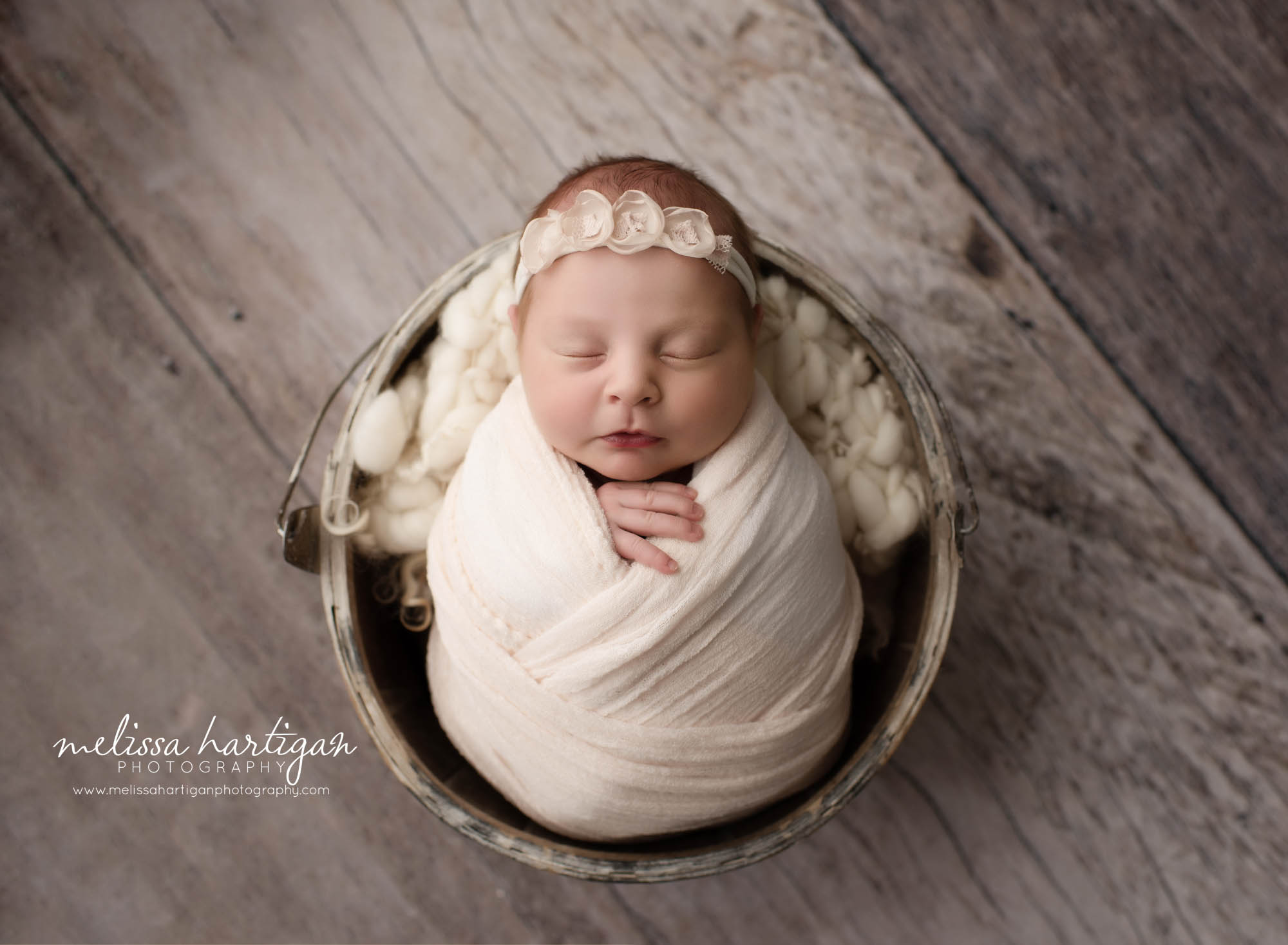 newborn baby girl posed in bucket wrapped in cream with flower headband