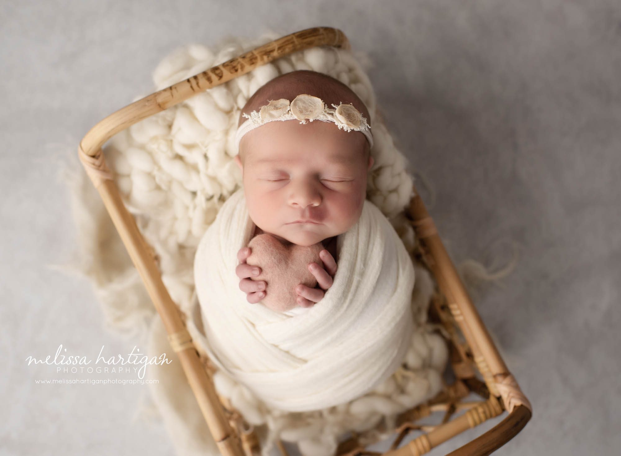 newborn baby girl wrapped in cream white wrap wearing headband holding pink felted heart prop Connecticut newborn photography