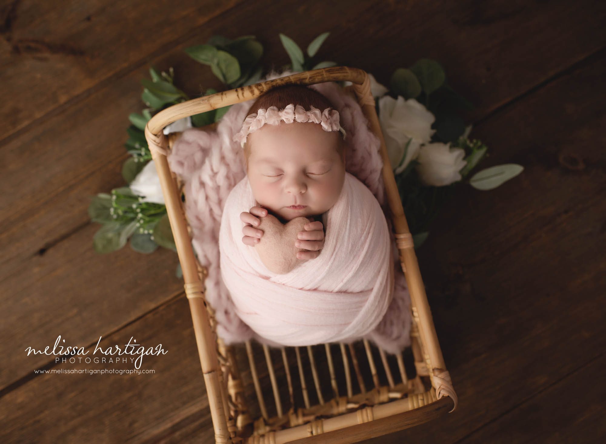 newborn baby girl wrapped in pink wrap posed in basket holding felted heart prop