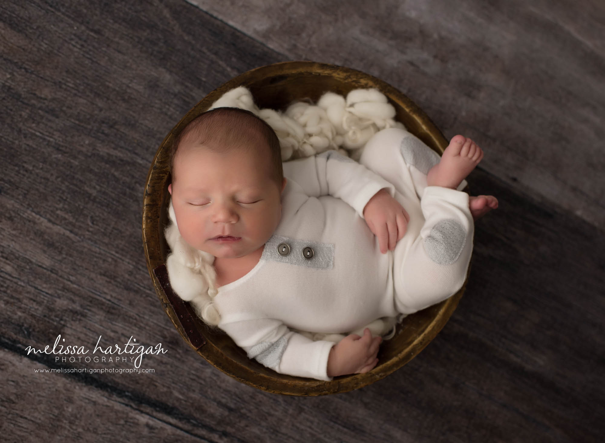 newborn baby boy wearing white newborn outfit posed in wooden bowl