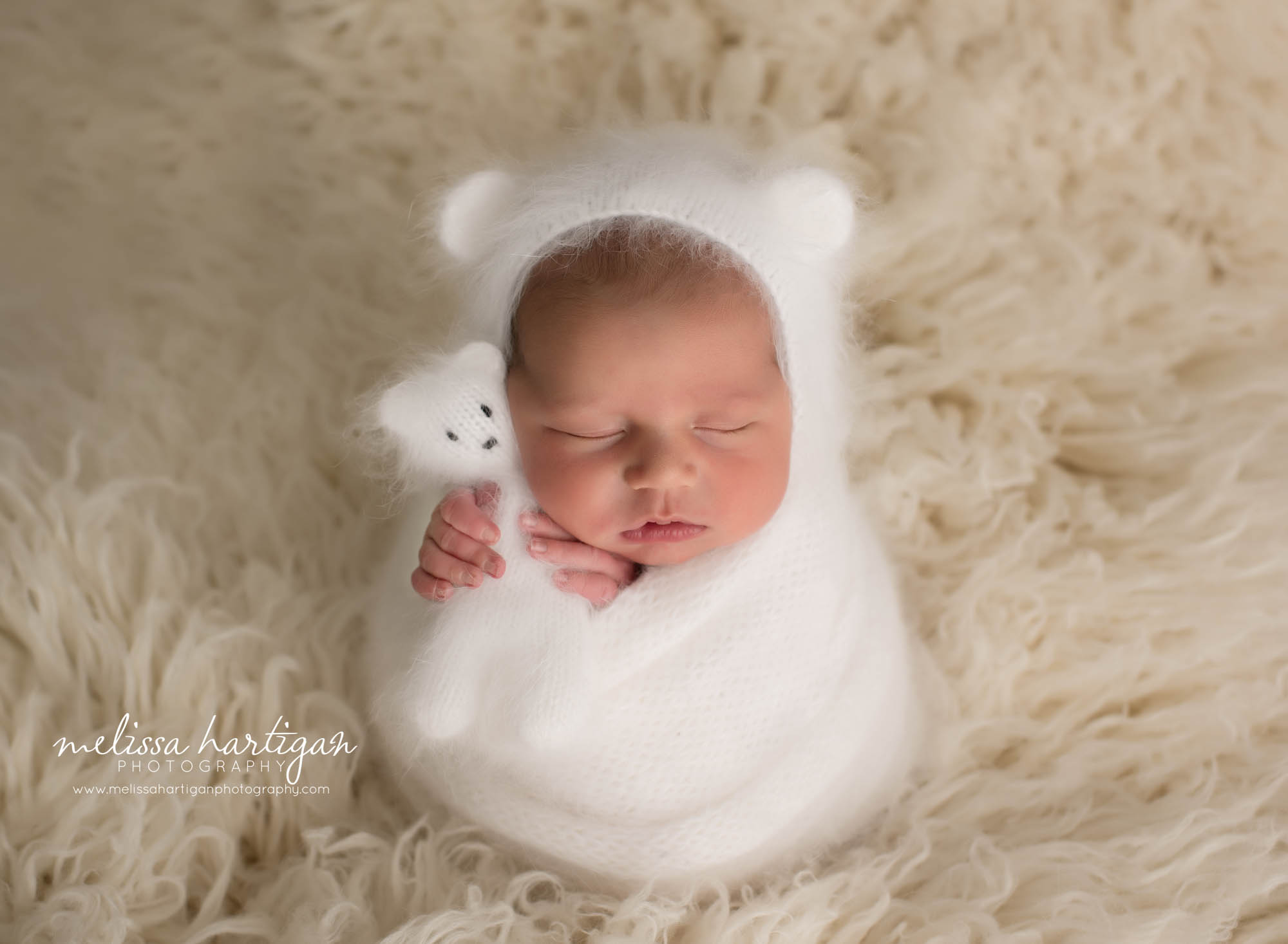 newborn baby boy wrapped in white knitted wrap holding knitted newborn teddy wearing matching knitted bear bonnet