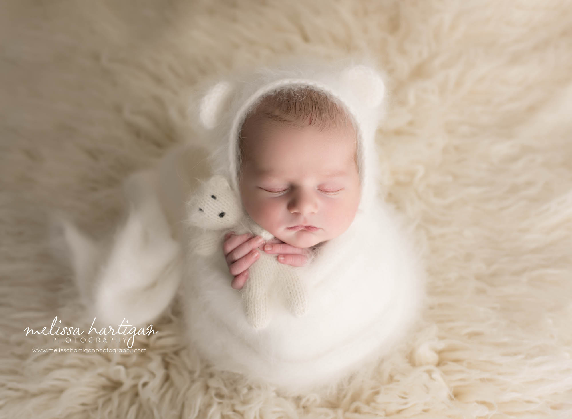 newborn baby boy wrapped in cream knitted wrap posed with knitted teddy bear prop wearing matching bear bonnet