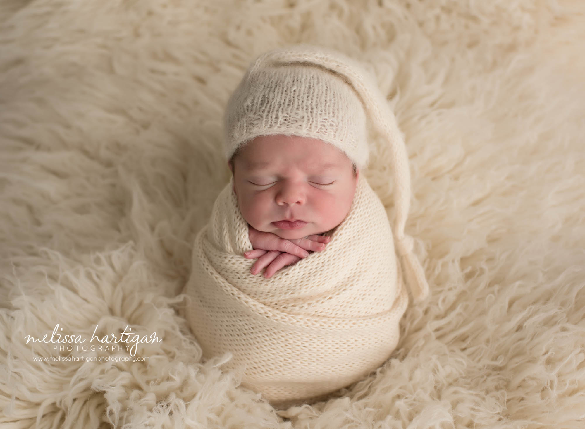 newborn baby boy wrapped in cream knitted wrap wearing knitted sleepy cap