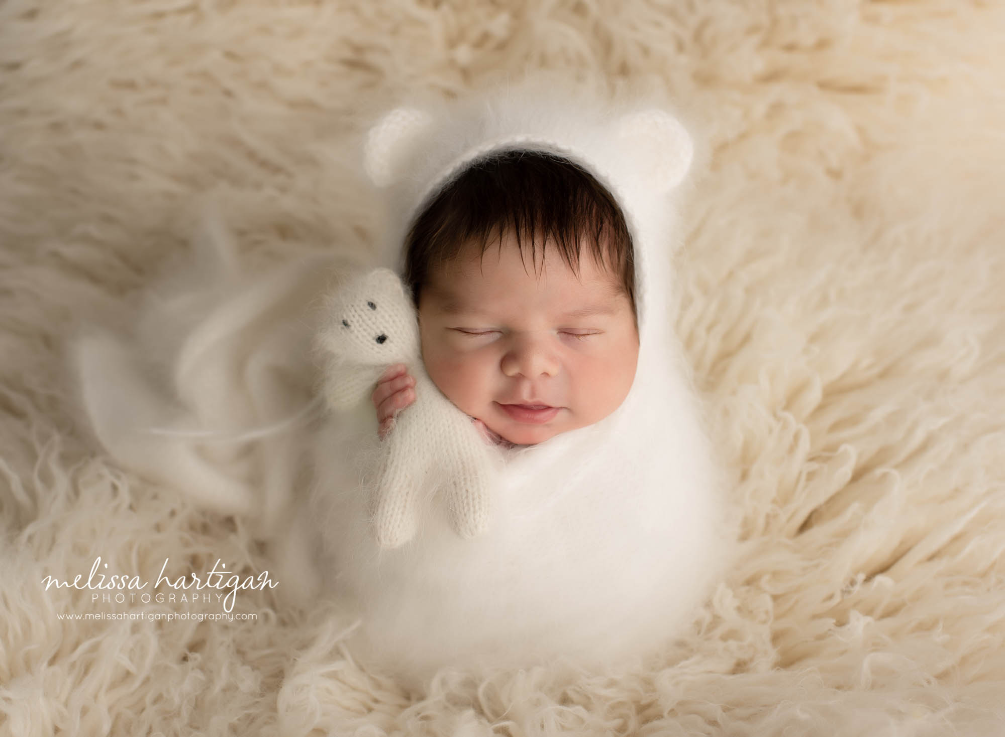 newborn baby boy wrapped in white cream knitted wrap wearing matching bonnet and holding knitted teddy bear smirk smiling CT newborn photographer