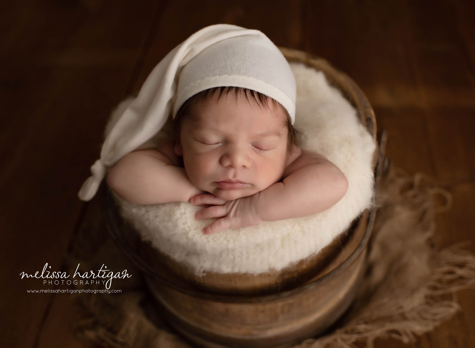 newborn baby boy posed in bucket wearing cream sleepy cap