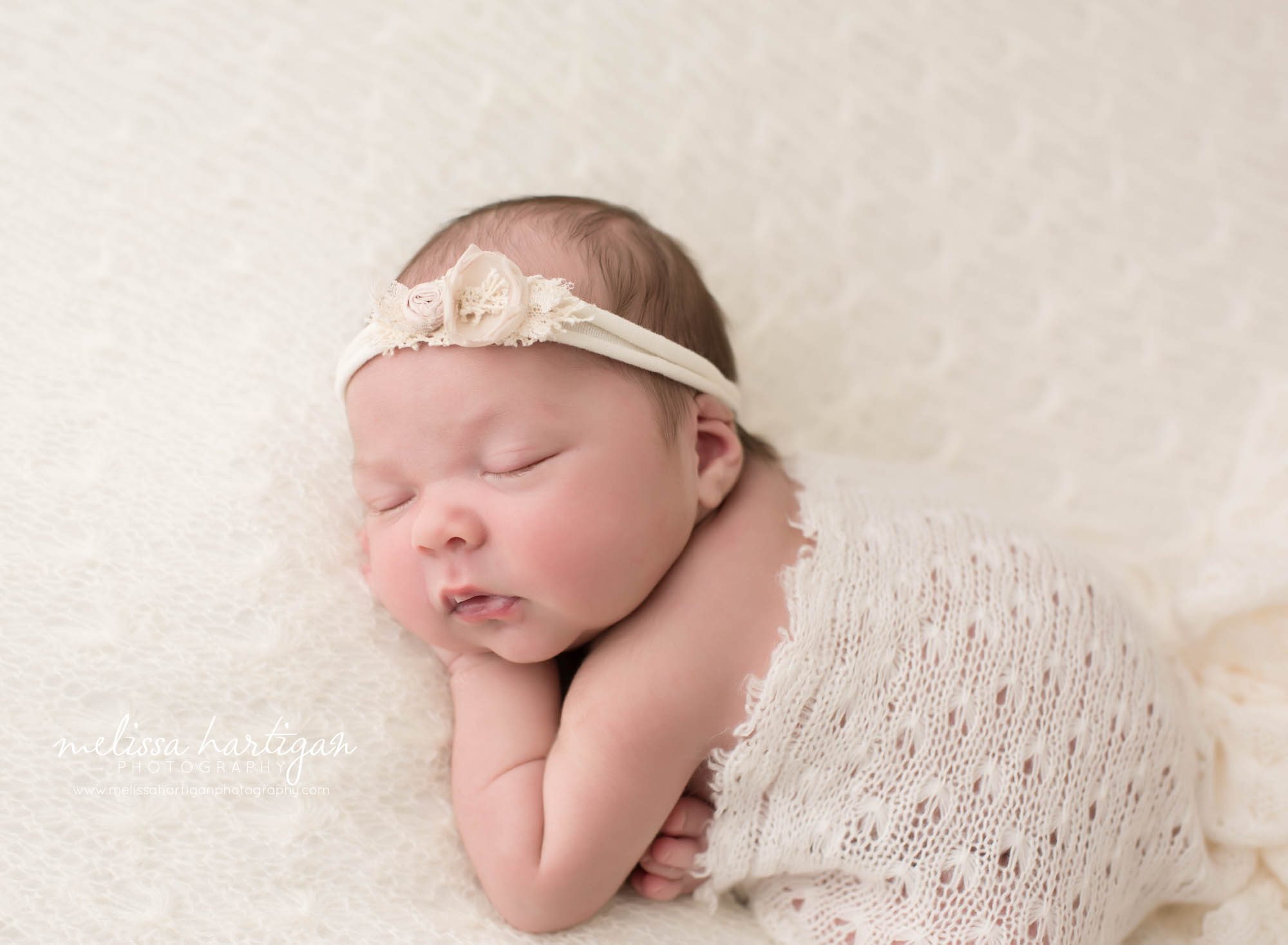 newborn baby girl posed on side with hand under cheek wearing flower headband with cream knit lace wrap draped over newborn baby photographer CT