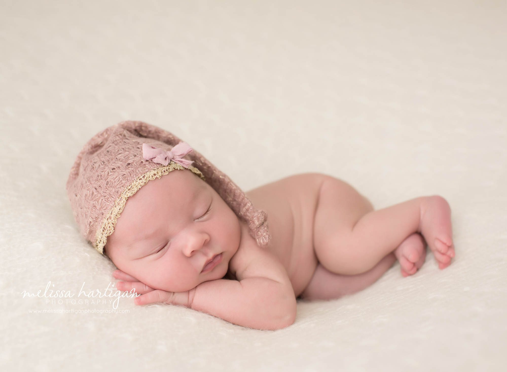 newborn baby girl posed on tummy side wearing pink sleepy cap