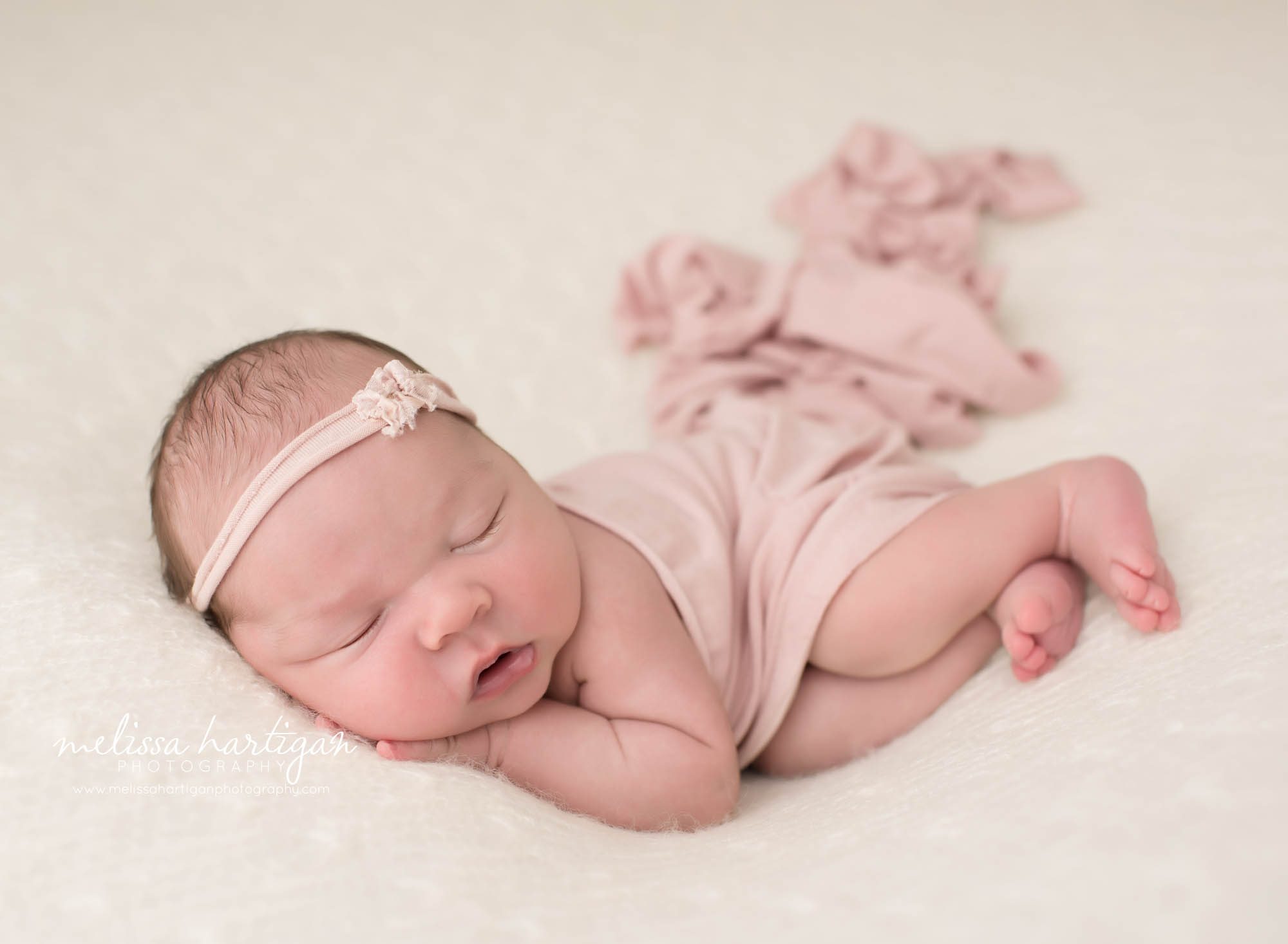 newborn baby girl posed on cream backdrop wearing pink headband with pink wrap draped over her newborn baby photography CT