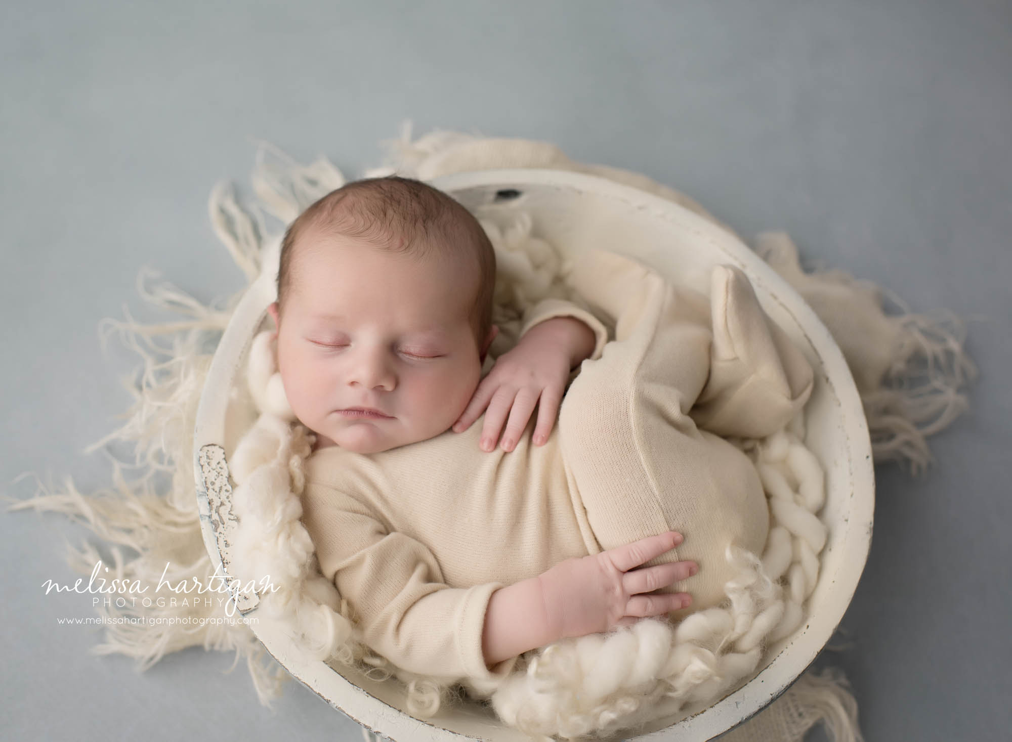 newborn baby boy posed in wooden bowl with cream colored fluff wearing cream outfit newborn photography connecticut