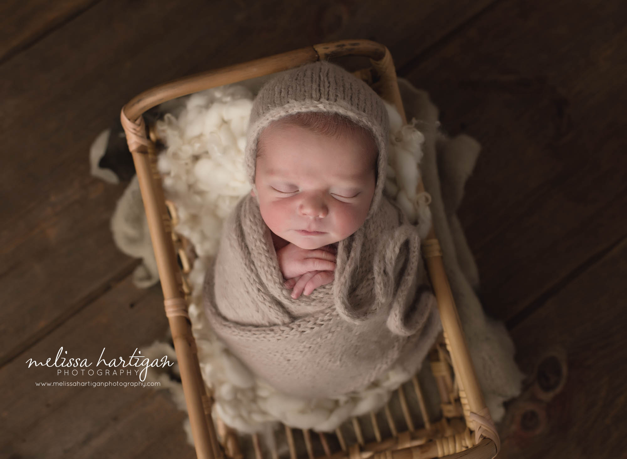 newborn baby boy wrapped in knitted wrap wearing matching bonnet posed in basket