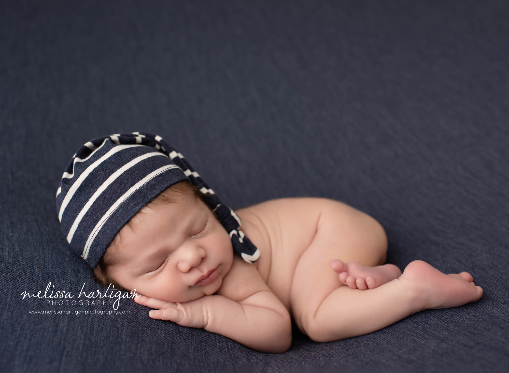 newborn baby boy posed on tummy wearing navy blue and white stripped sleepy cap