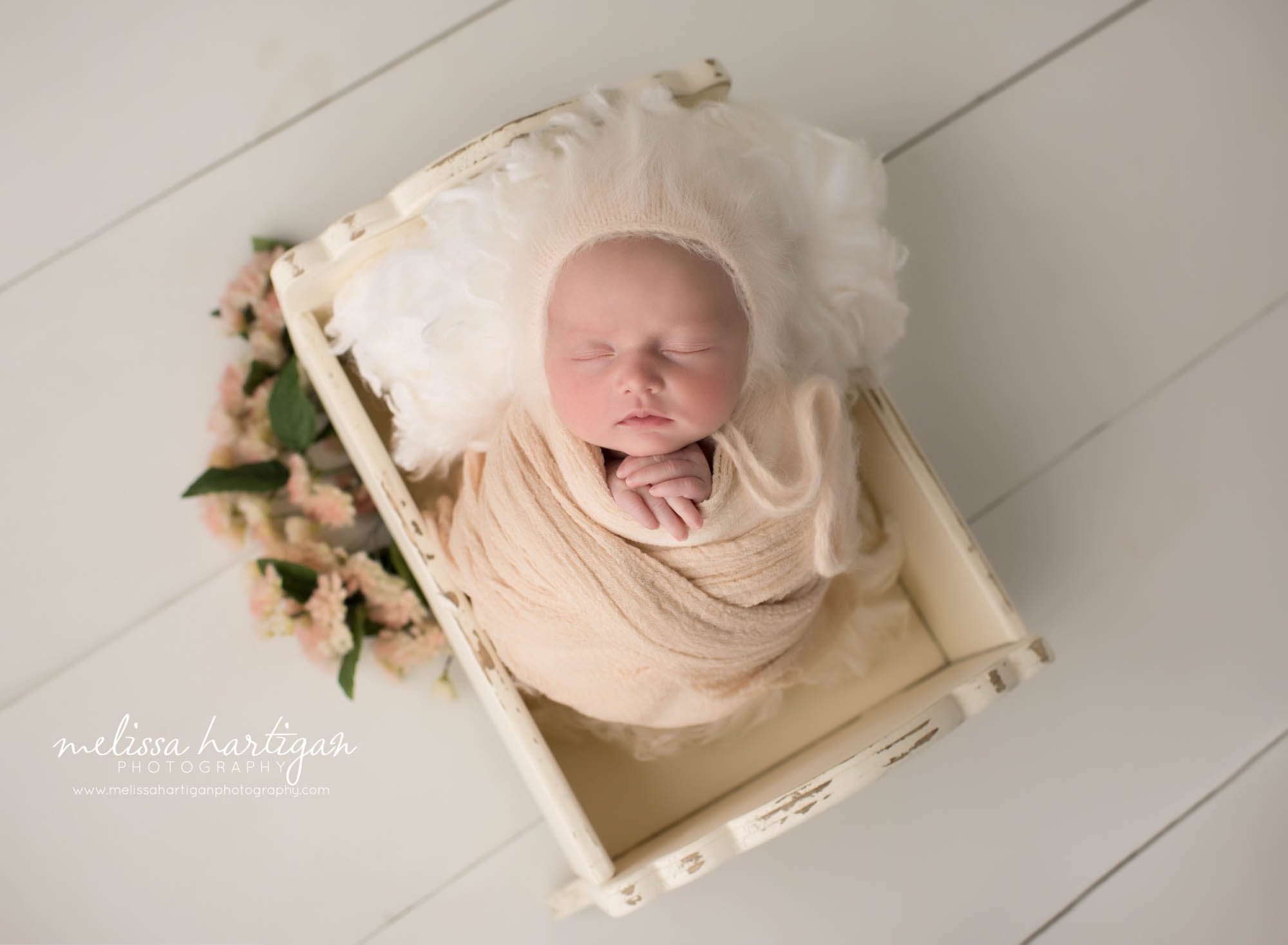 newborn baby girl posed in wooden newborn cradle prop wrapped in peach color