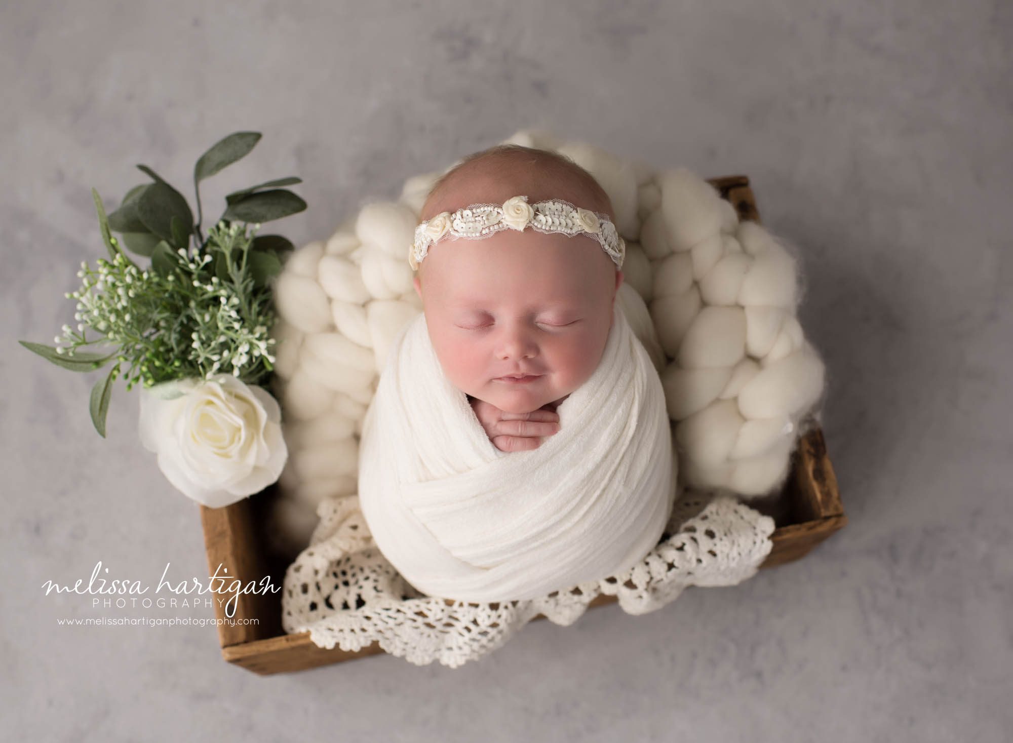 newborn baby girl wrapped in white wrap posed in wooden prop with white layers