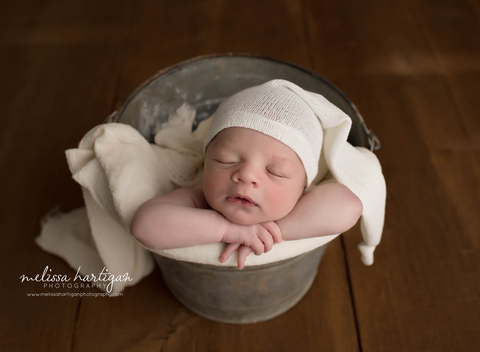 newborn baby boy posed in bucket wearing cream colored sleepy cap newborn photographer Suffield CT
